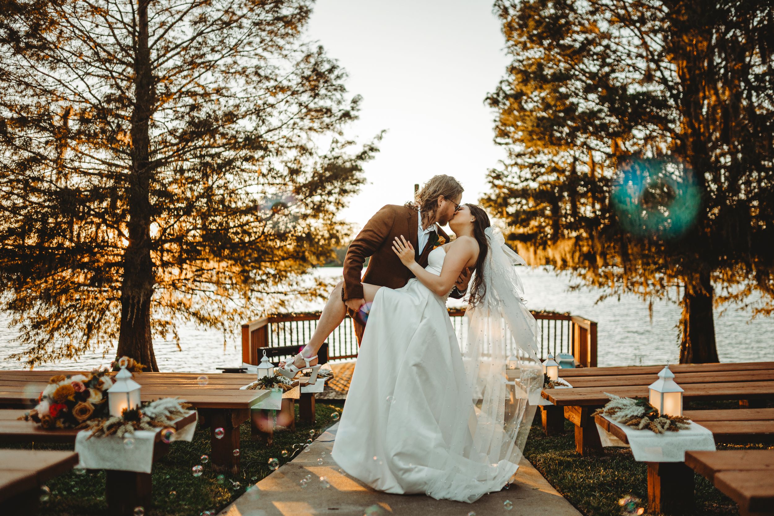 Sunset wedding ceremony by the lake with decorated wooden benches.