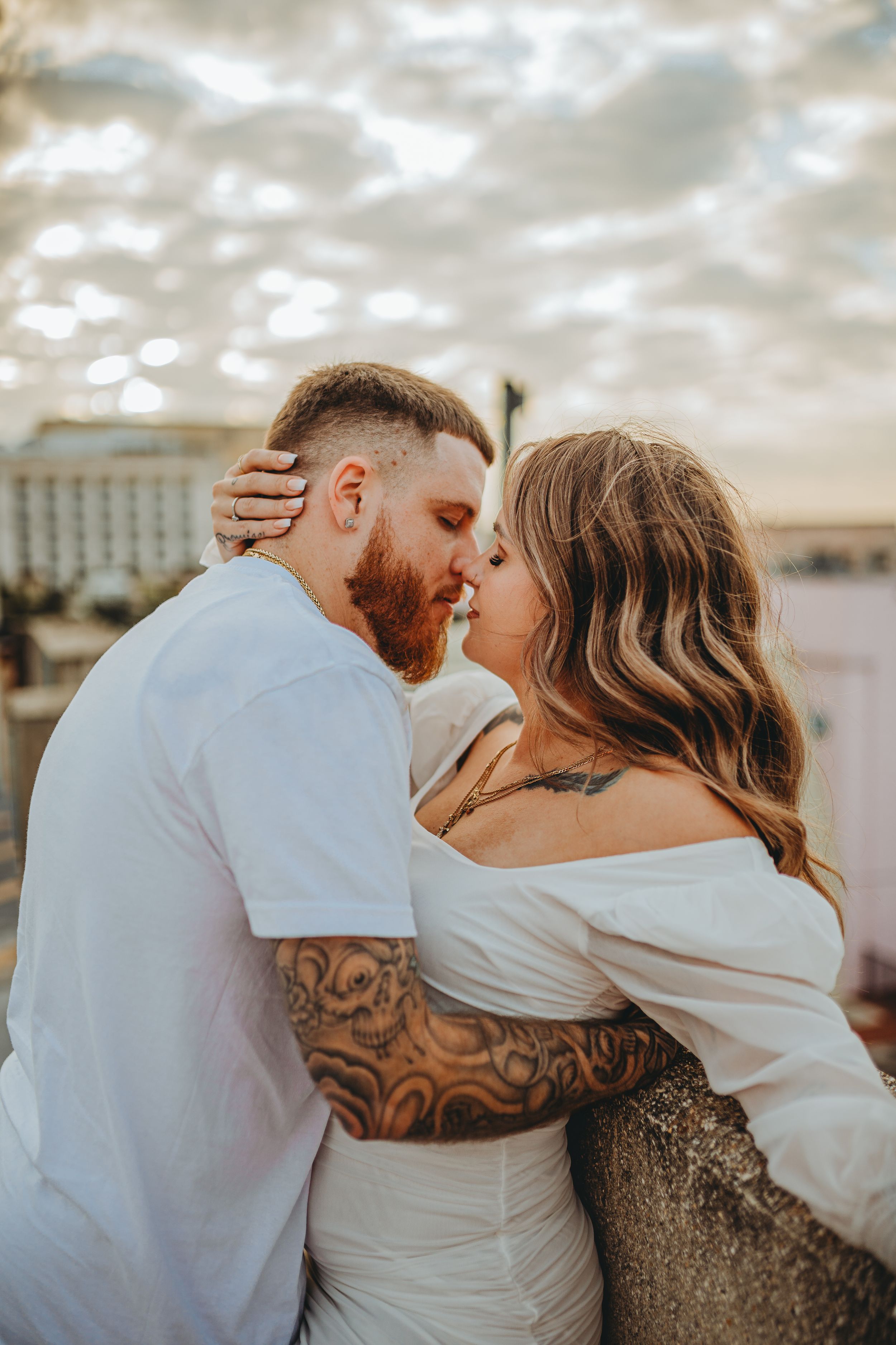 Intimate sunset portrait of couple embracing on rooftop with dramatic cloudy sky.