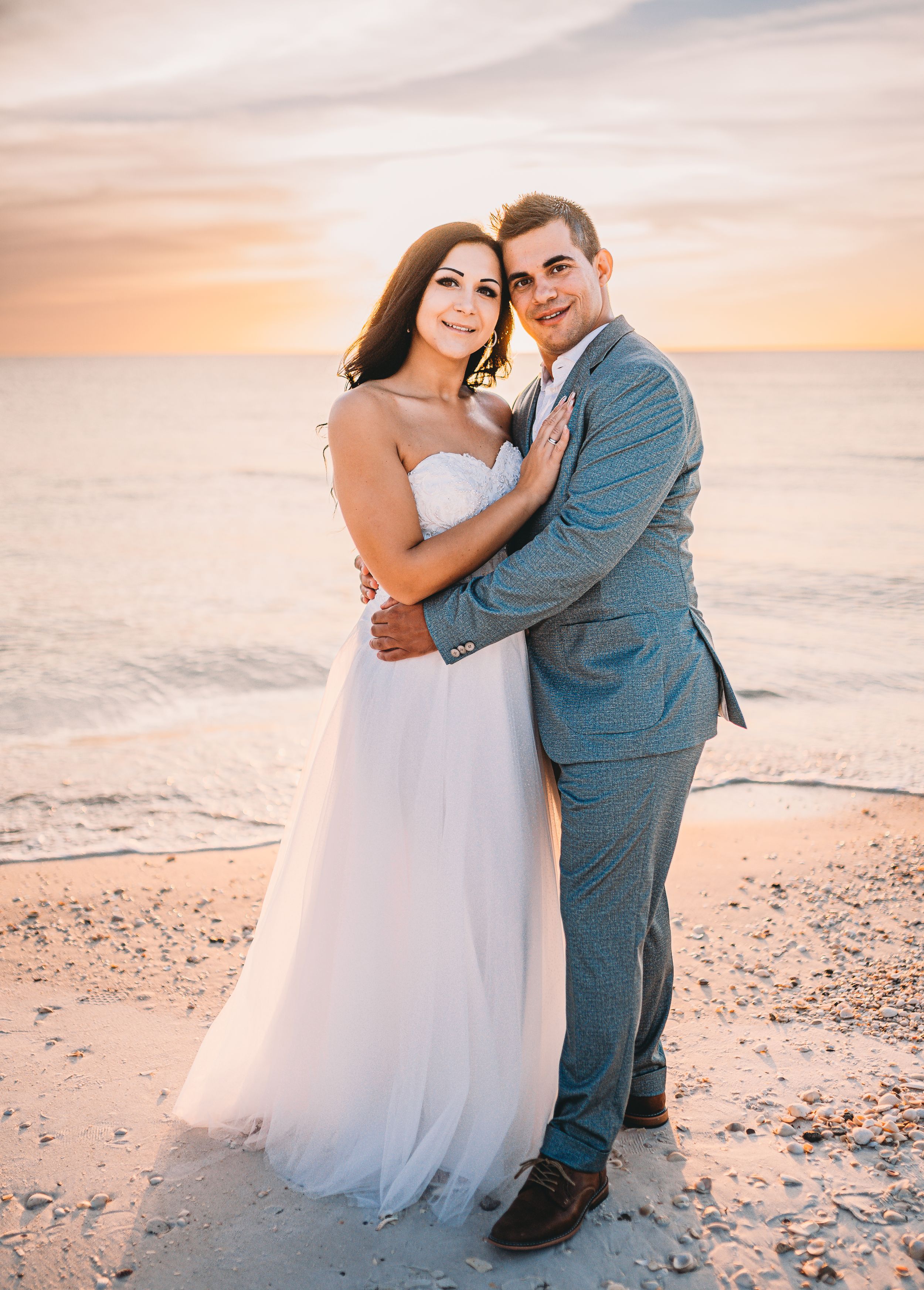 Romantic beach wedding portrait at sunset with couple in formal attire.