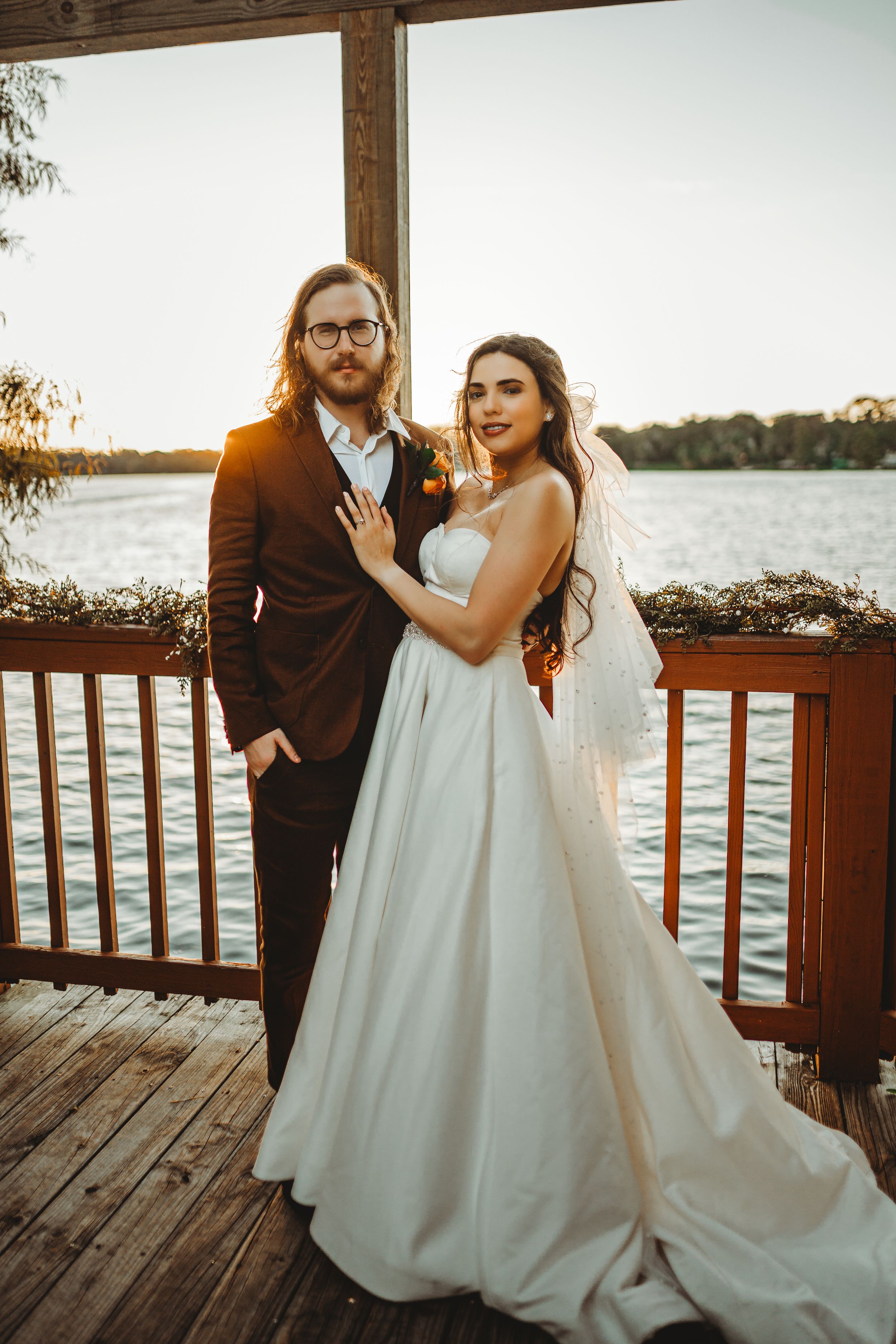 Newlyweds pose together on lakeside deck during sunset photo session.