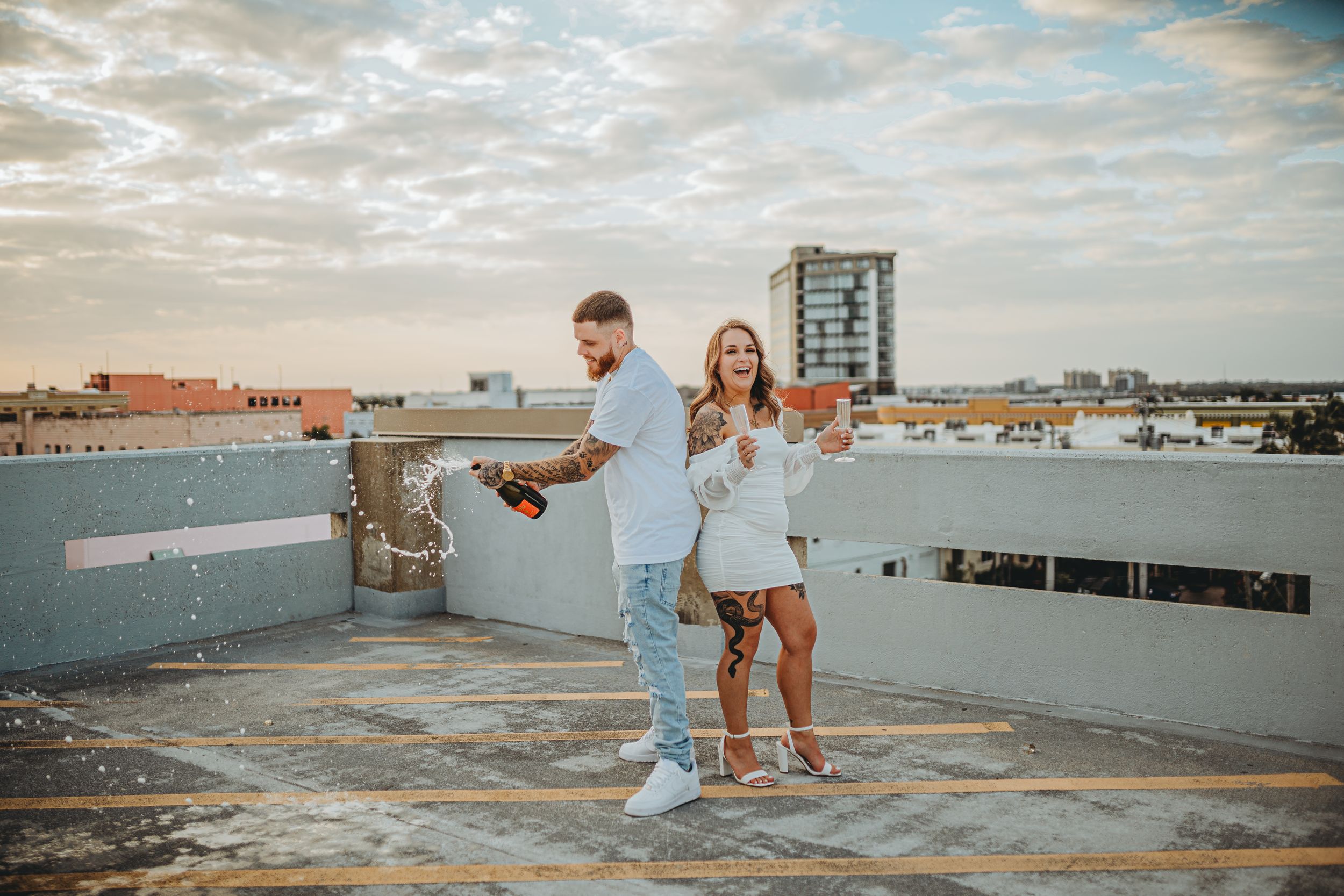 Playful couple dancing on urban rooftop during sunset photoshoot.