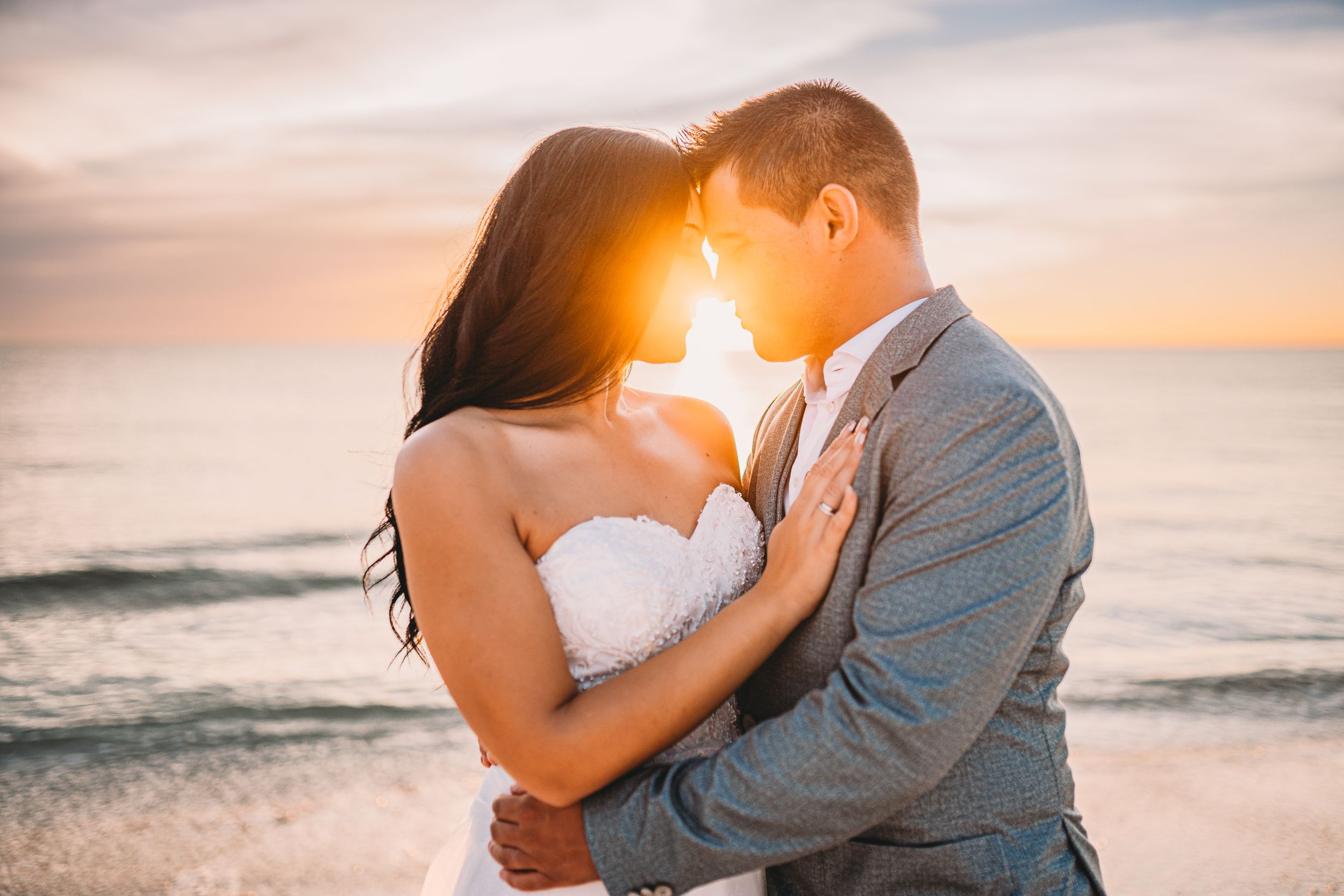 Romantic couple embraces on beach at sunset with golden light streaming between them.