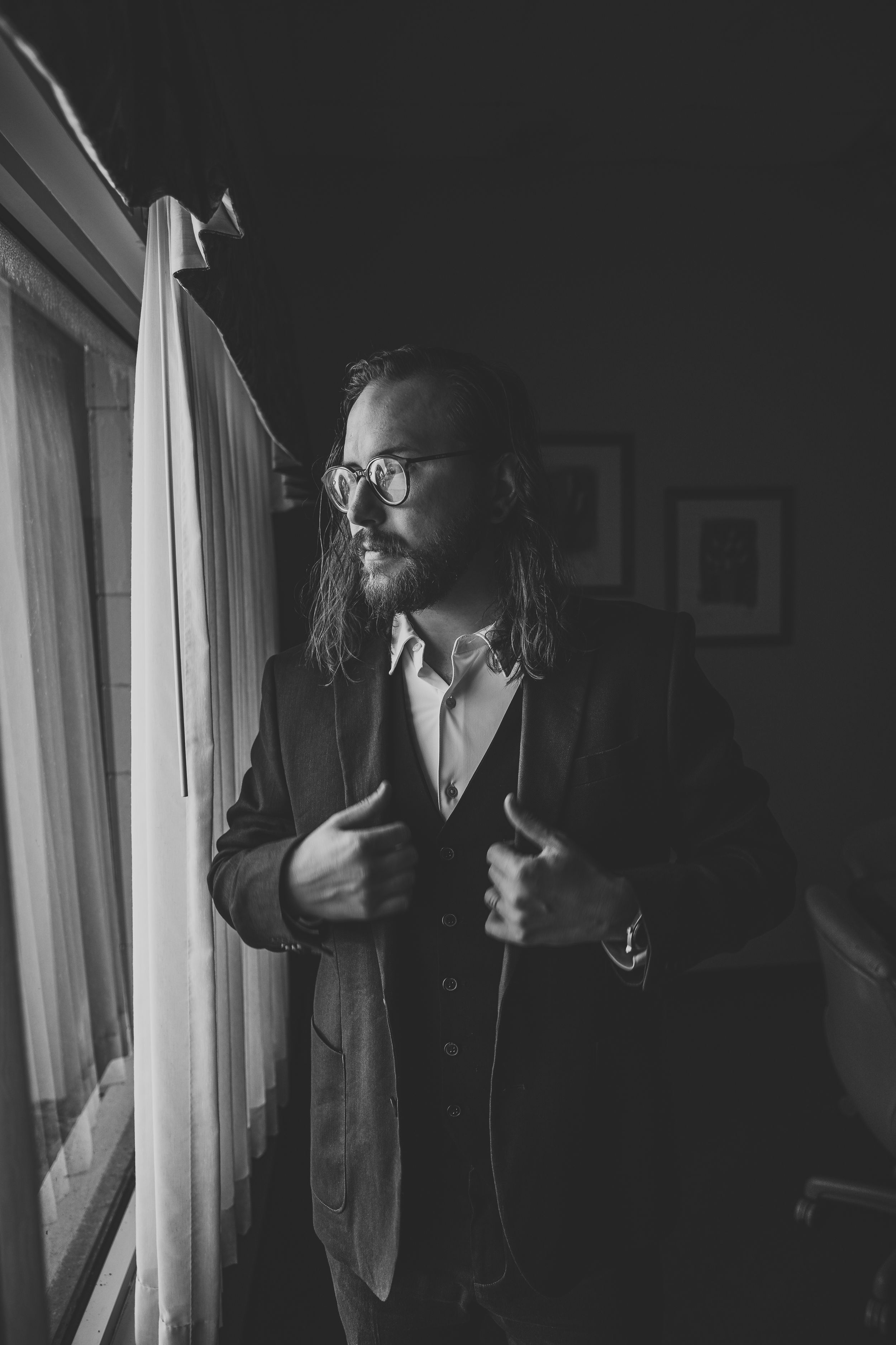 Dramatic black and white portrait of person in formal attire by window light.
