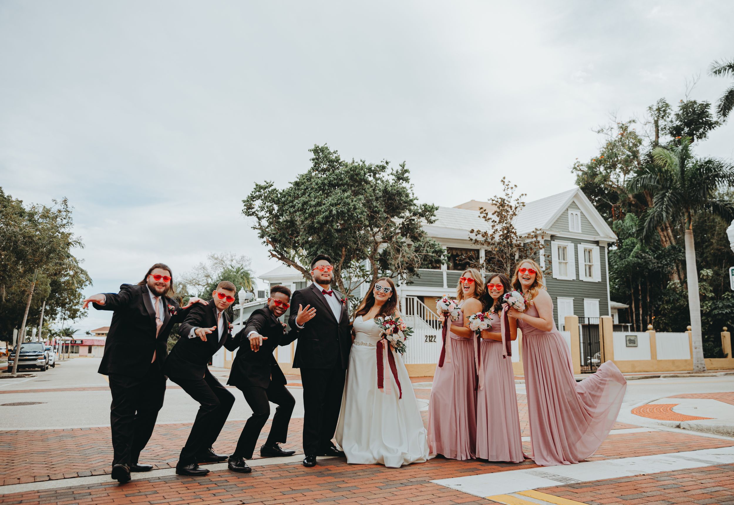 Wedding party poses playfully on brick walkway with bridesmaids in pink dresses.