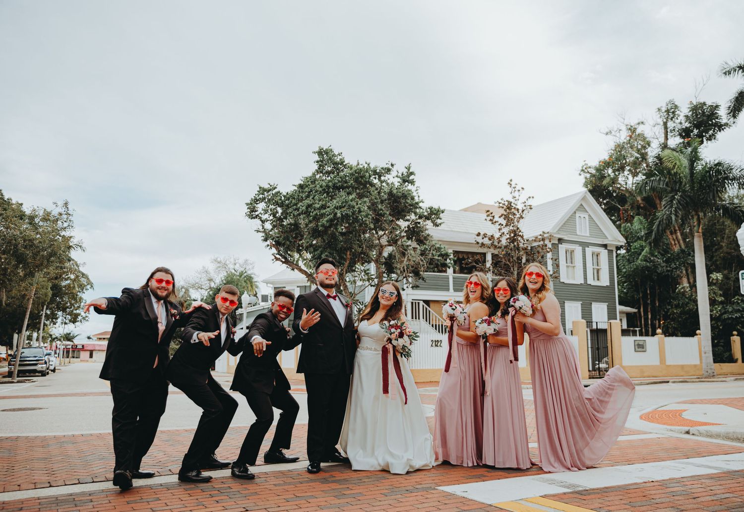 Wedding party poses playfully on brick walkway with bridesmaids in pink dresses.