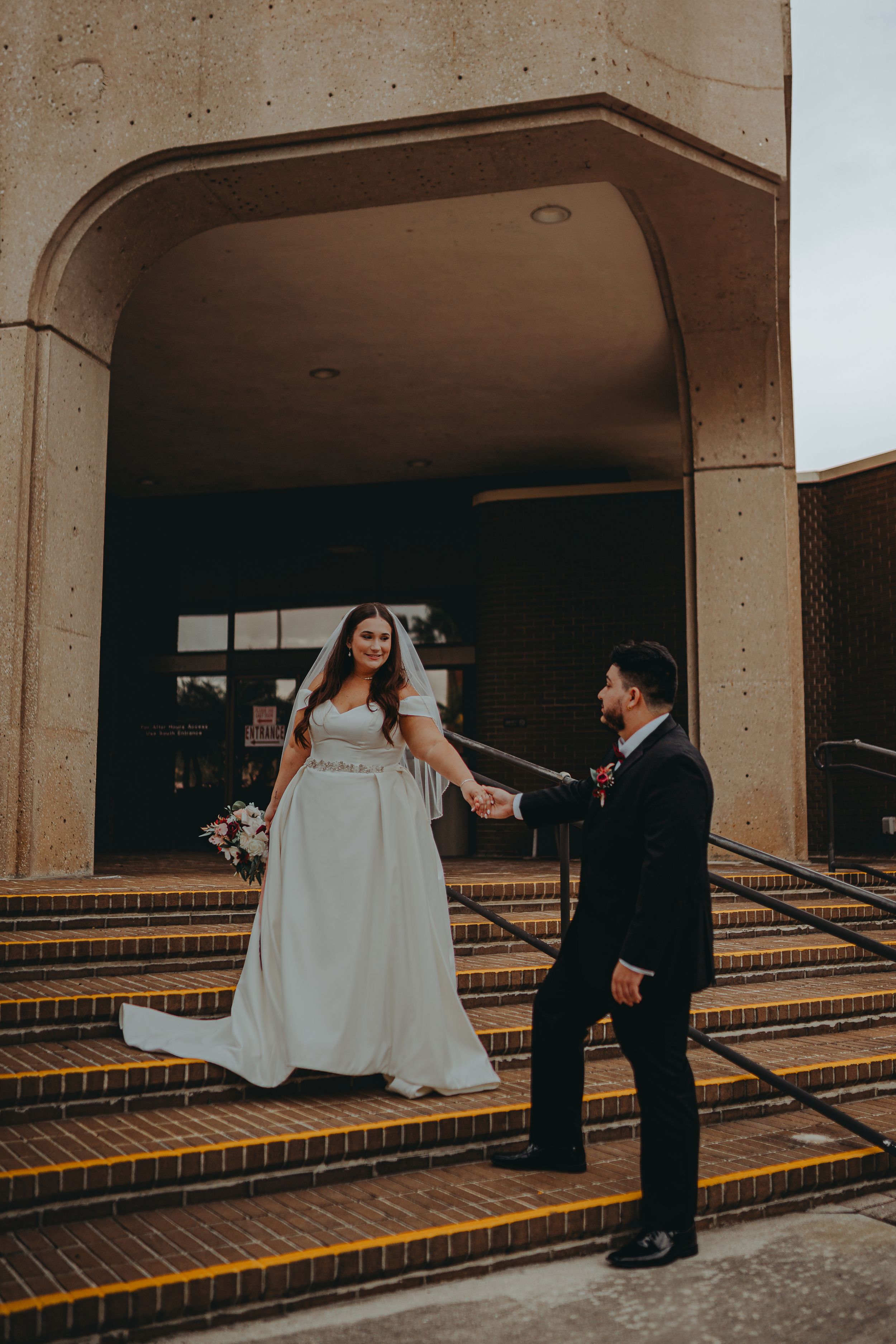 Bride and groom hold hands on concrete steps during wedding photoshoot.
