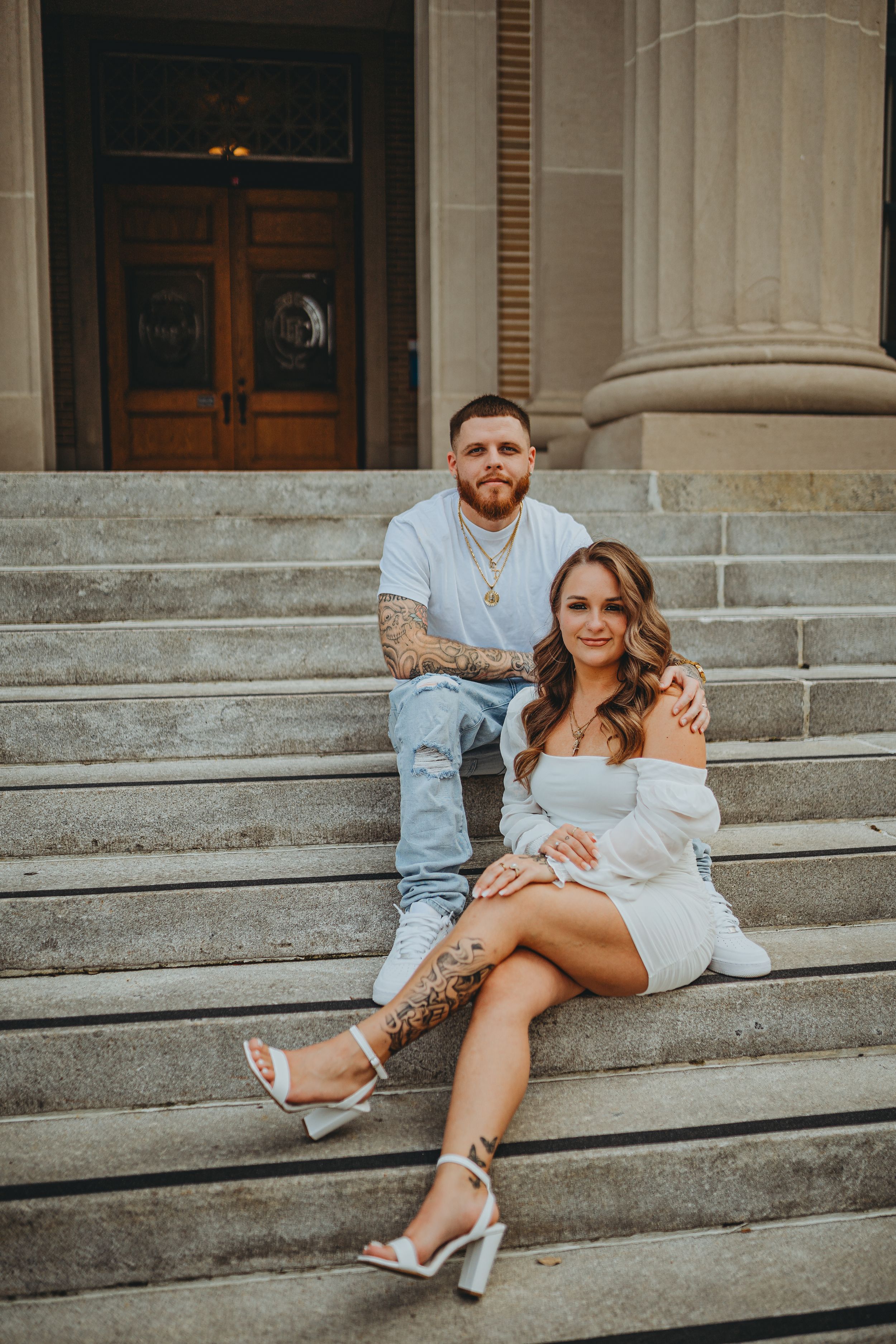 Stylish couple posing on grand stone steps of historic building.