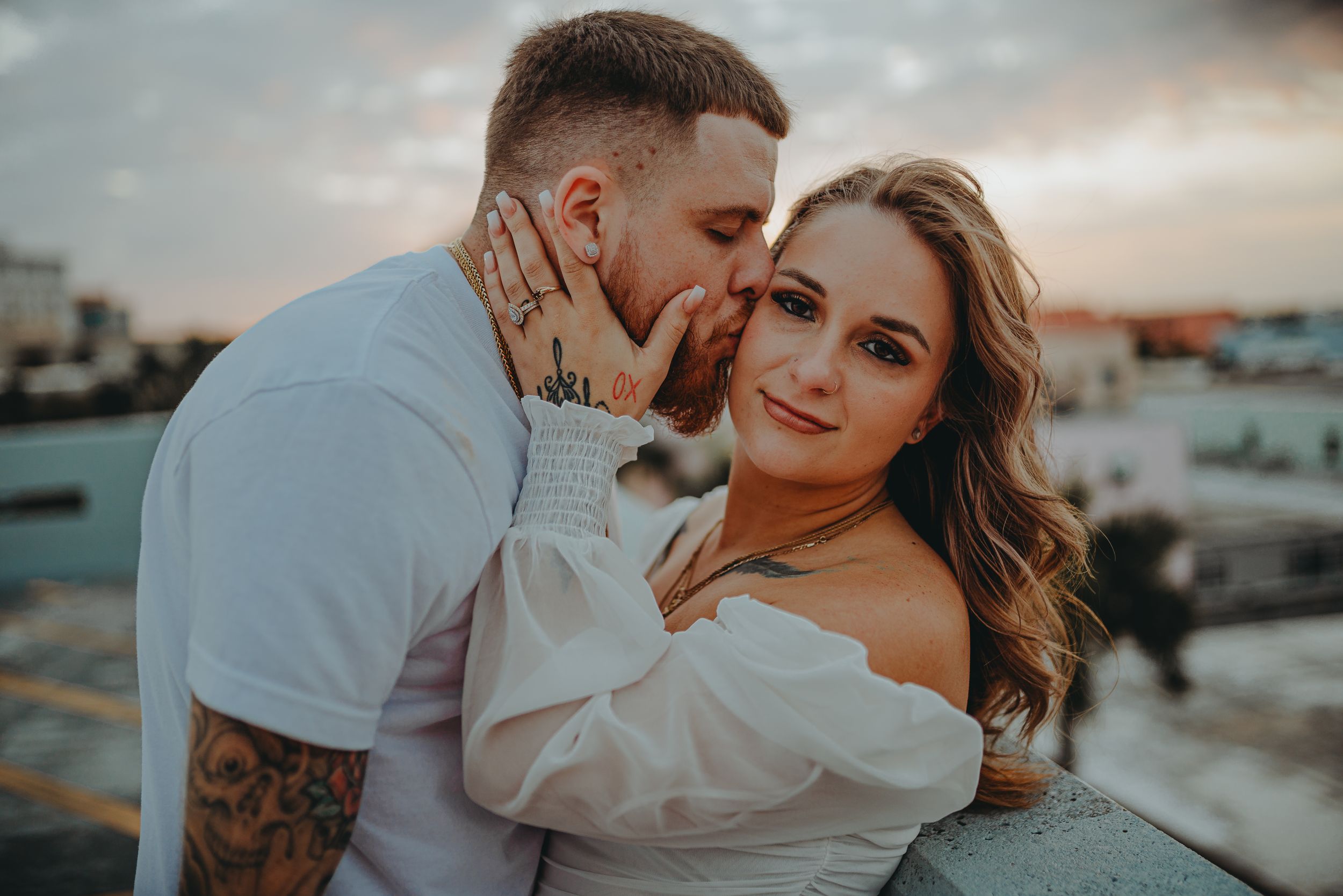 Sweet couple portrait on city rooftop with warm sunset lighting and urban skyline.