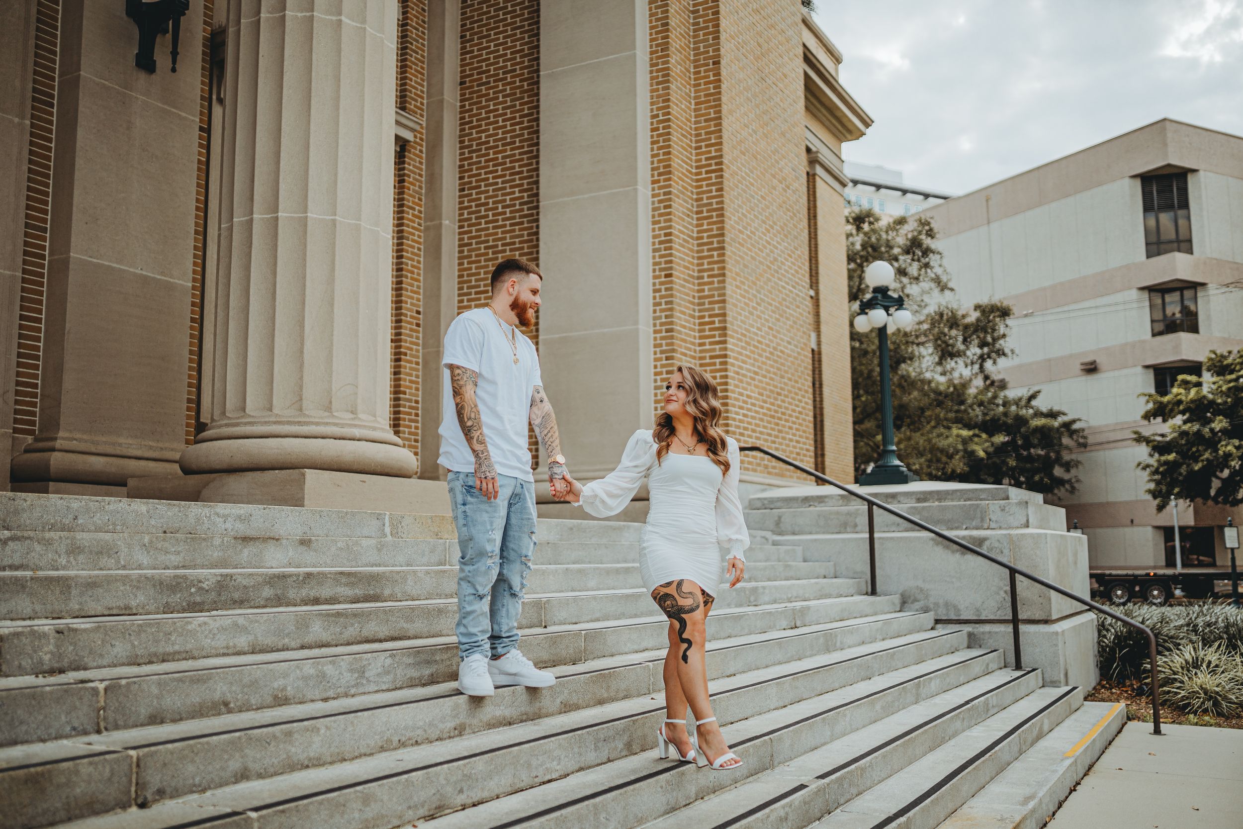 Couple holding hands while walking down classical stone steps in casual attire.