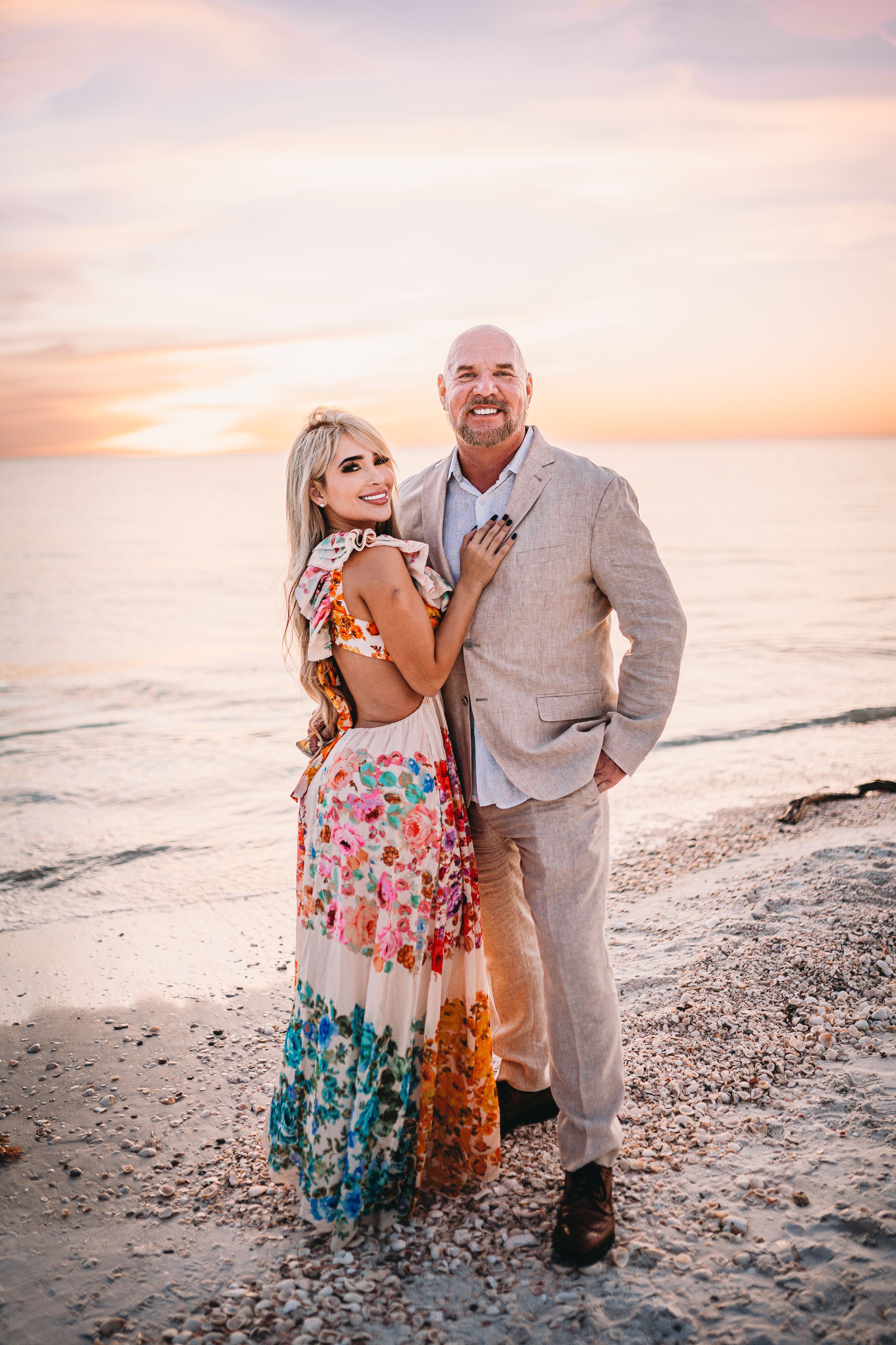 Couple poses together on beach at sunset wearing formal attire.