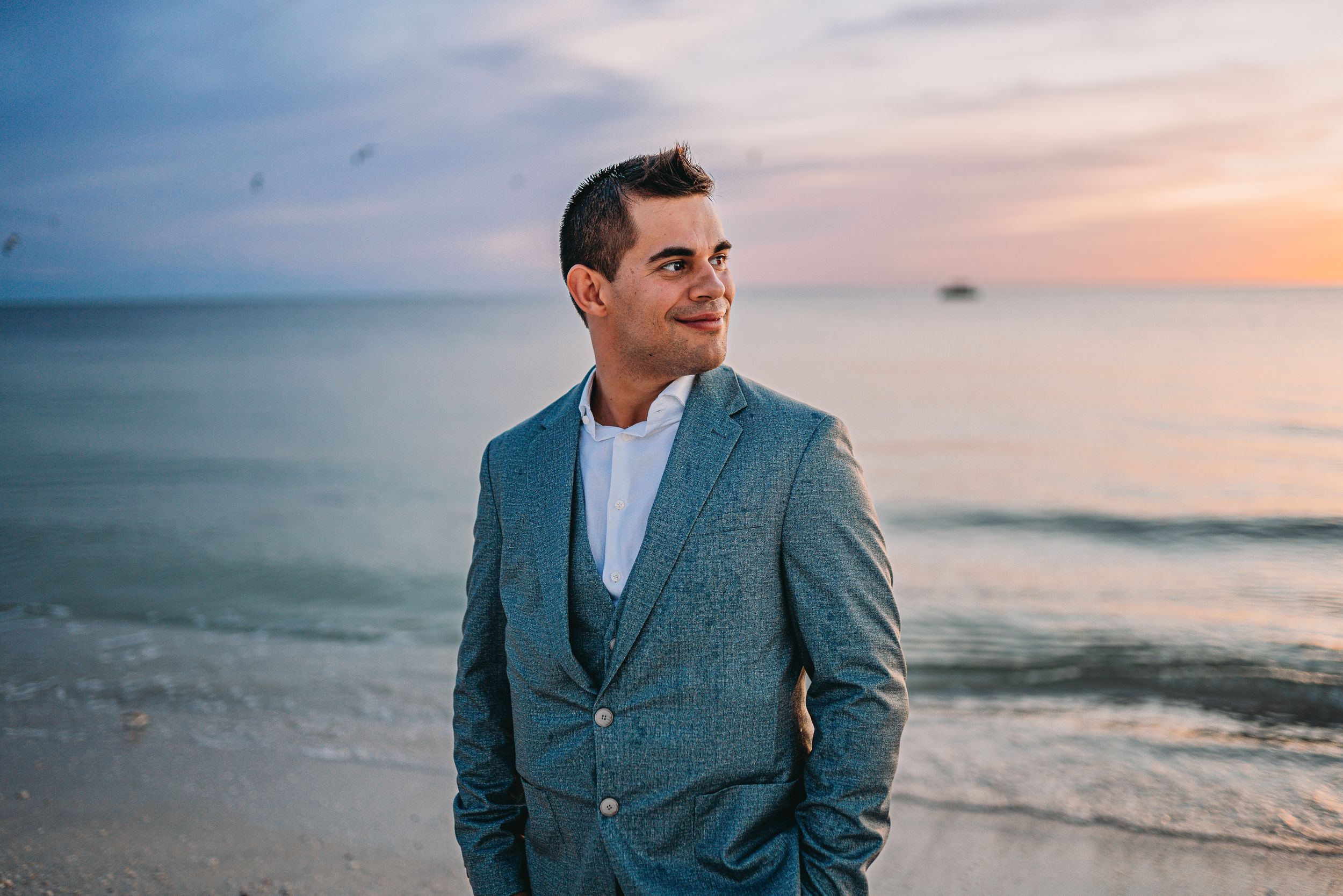 Well-dressed man in blue blazer gazes at ocean during sunset.