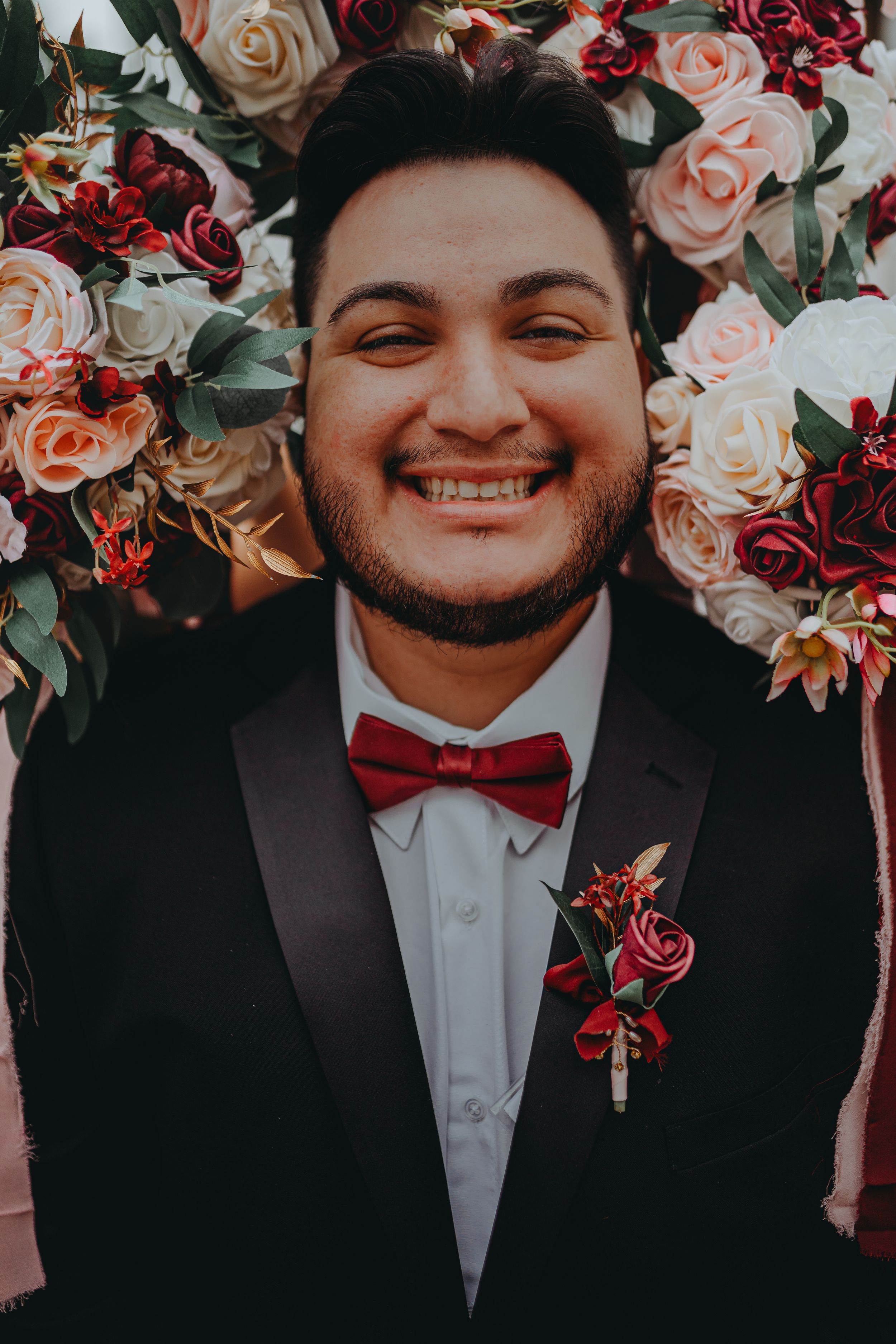 Wedding portrait with red and pink rose floral backdrop and red bowtie.