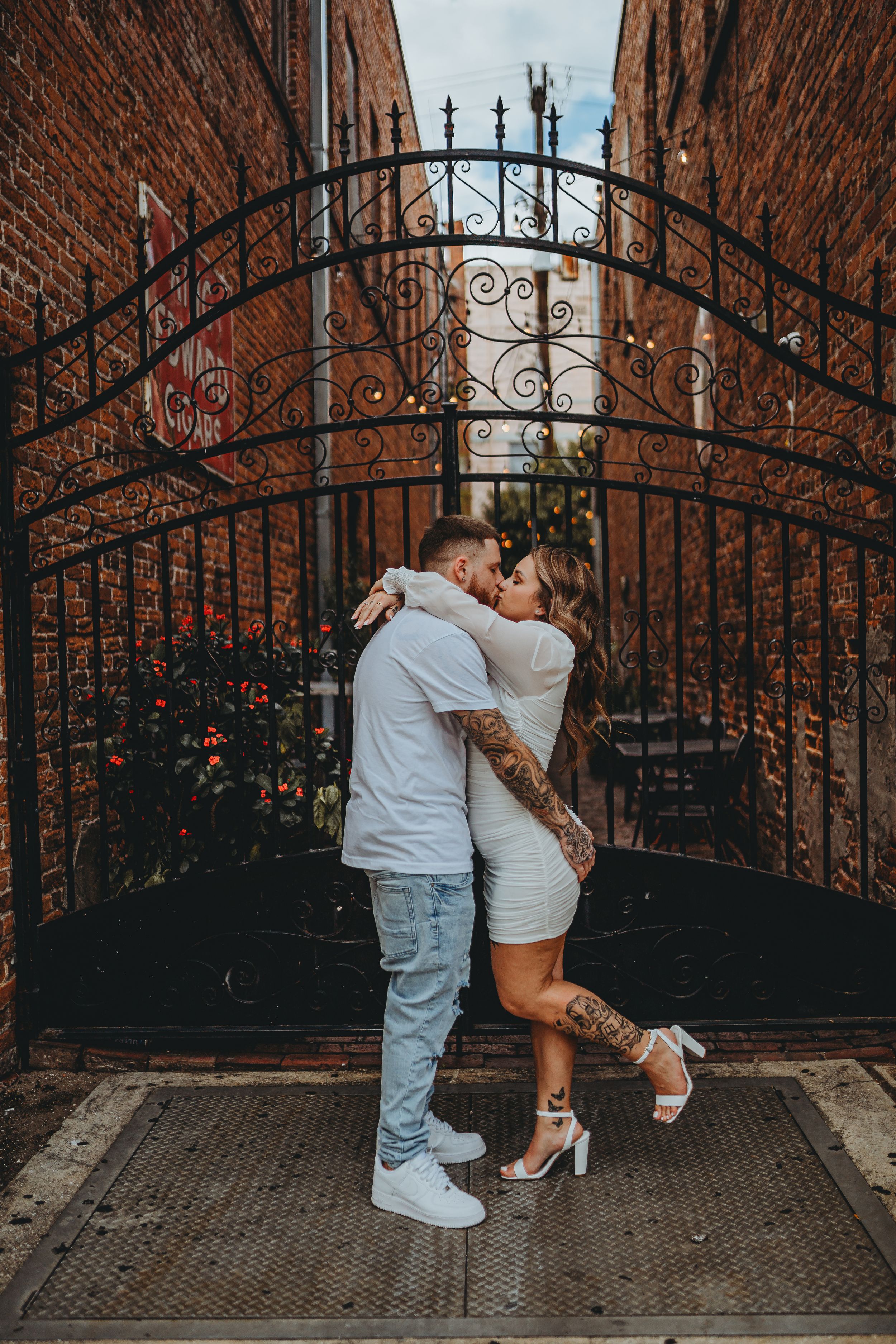 Romantic couple embracing in front of ornate wrought iron gate.