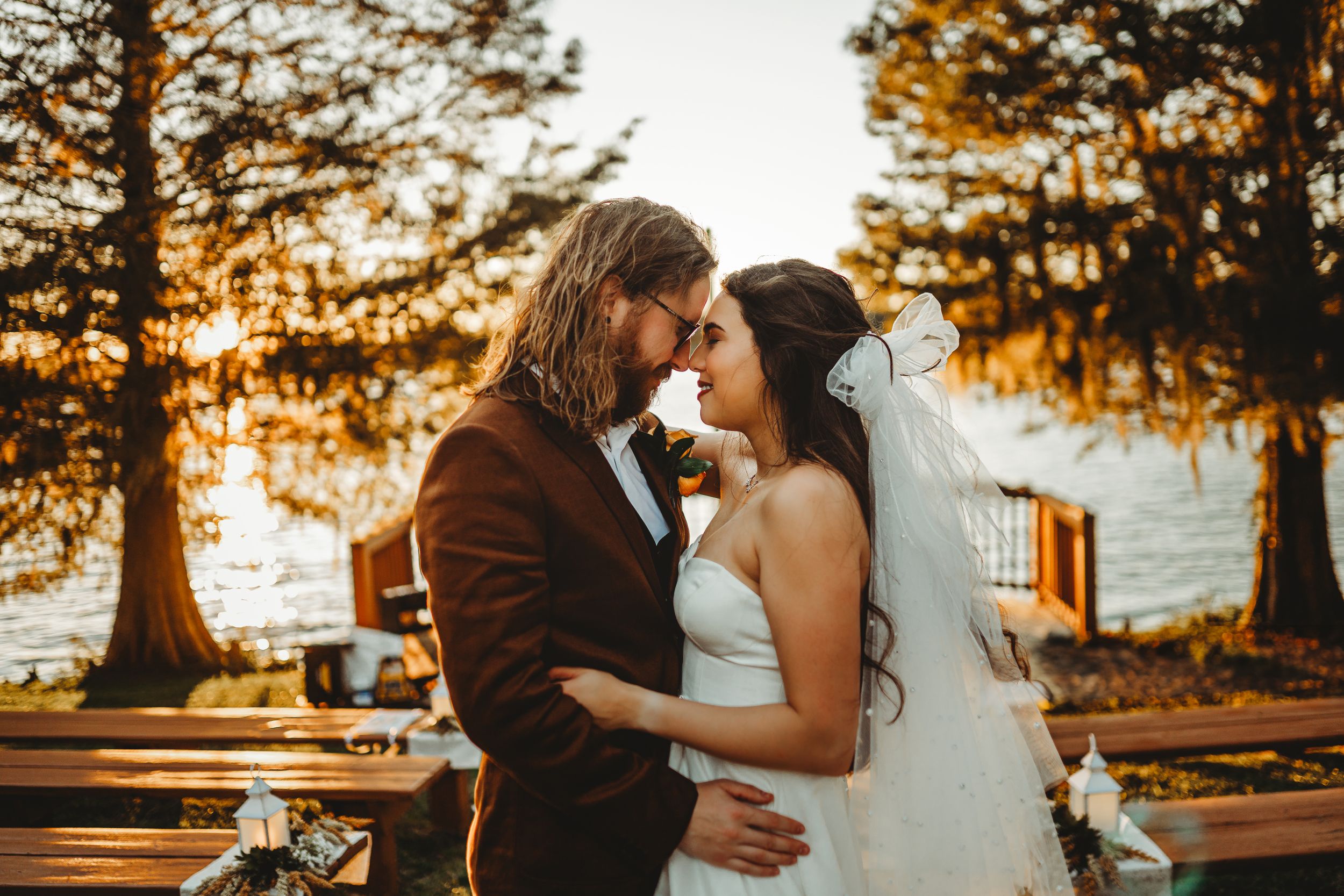 Intimate lakeside wedding scene with cypress trees at sunset.
