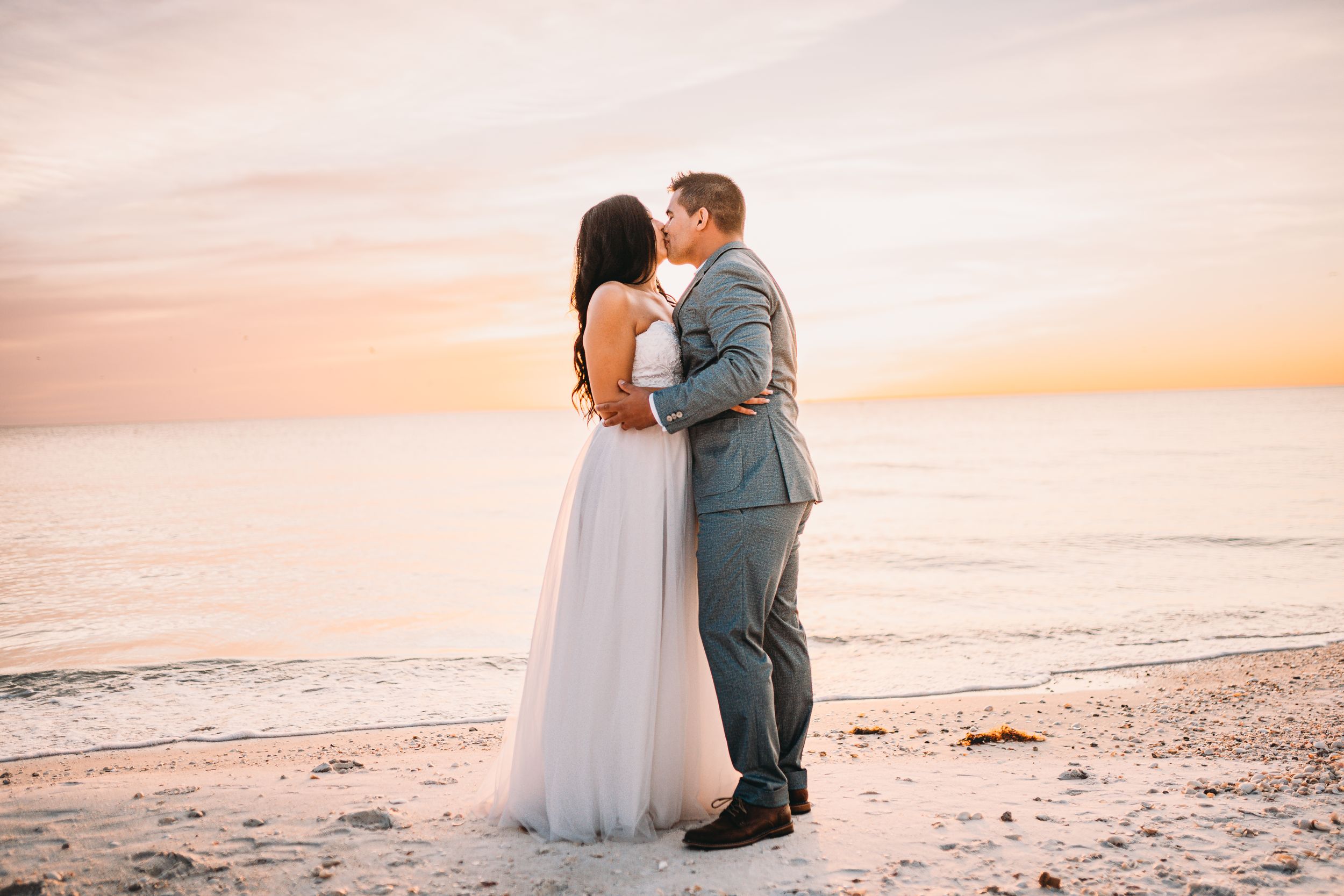 Elegant couple in wedding attire share intimate moment on beach at dusk.