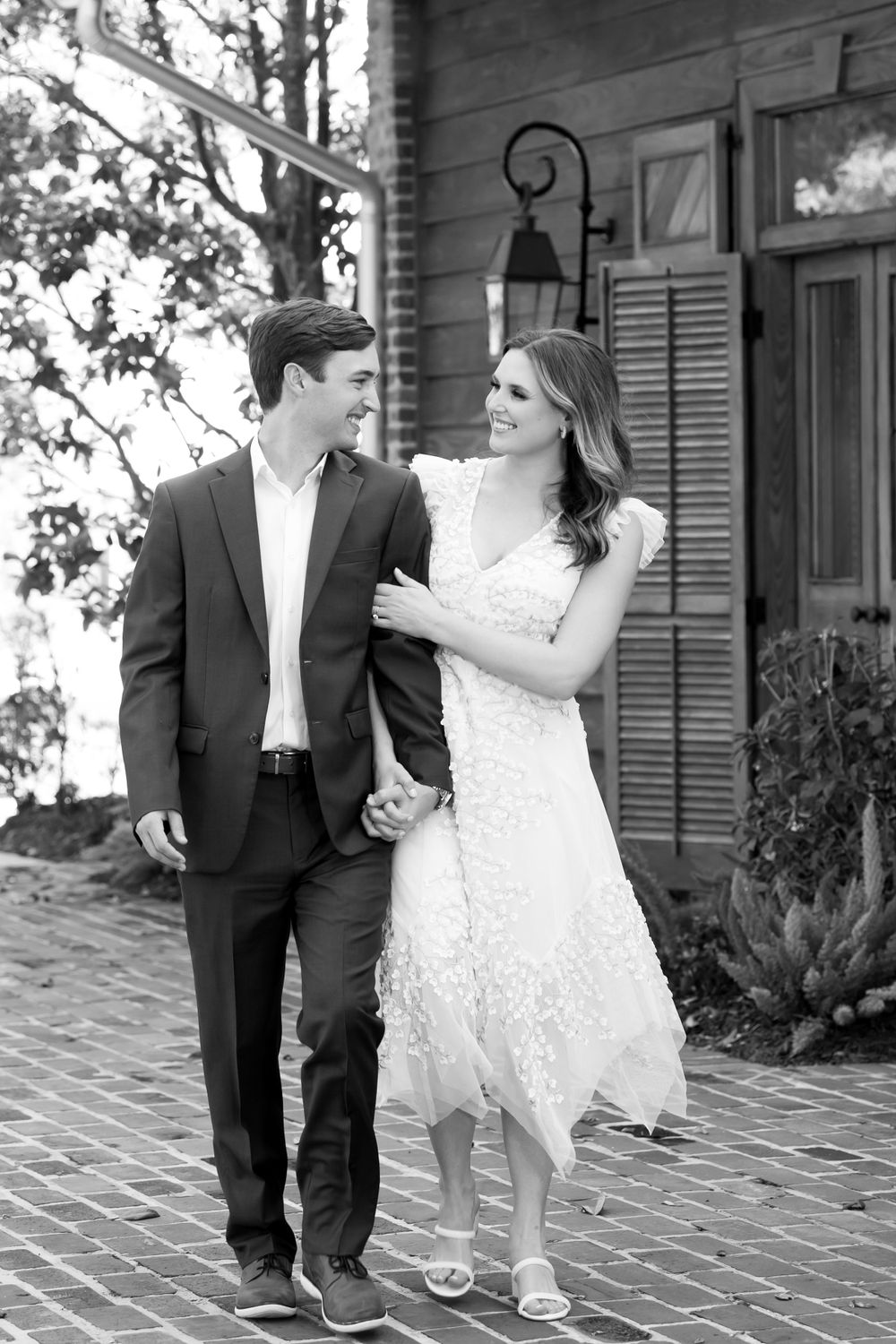 Couple shares playful moments on a brick patio with rustic shutters in the background.