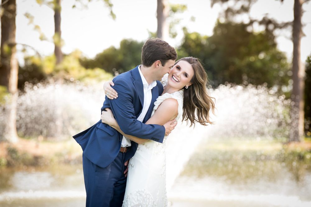 Romantic wedding couple embraces in golden sunlight among pine trees.