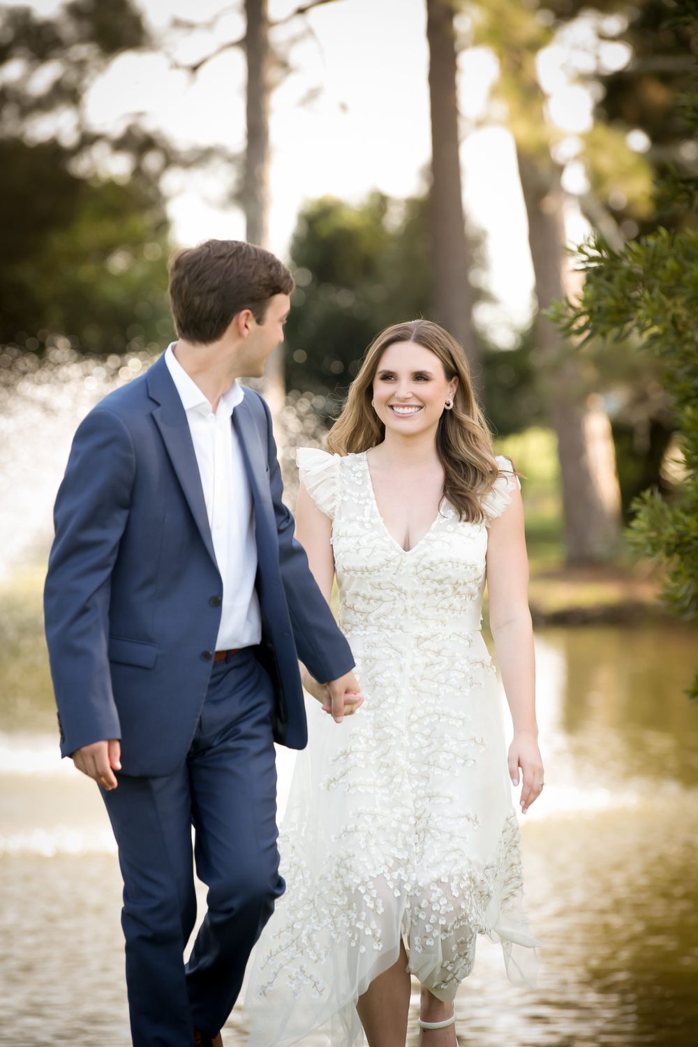 Wedding couple poses together by a lake at sunset with trees in the background.
