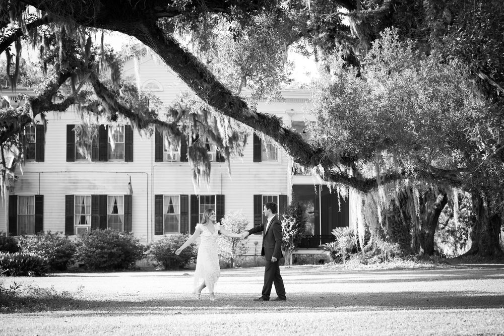 Historic white plantation house with black shutters and large oak trees.
