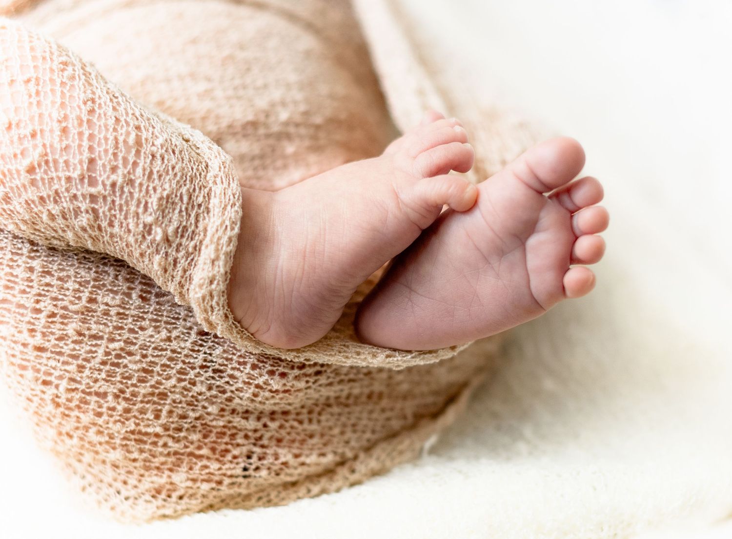 Close-up series of tiny newborn baby feet wrapped in soft beige knit fabric.
