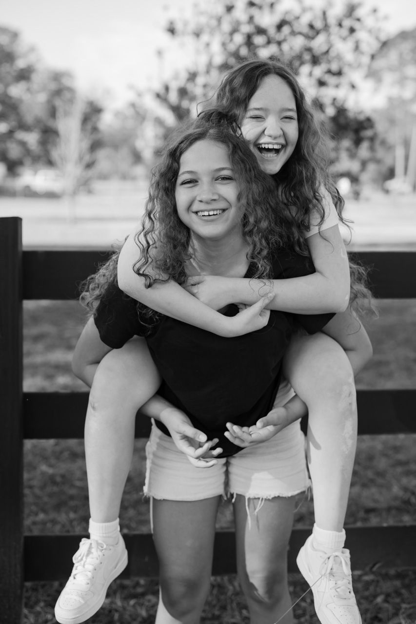 Two people share playful piggyback rides outdoors in black and white photography.