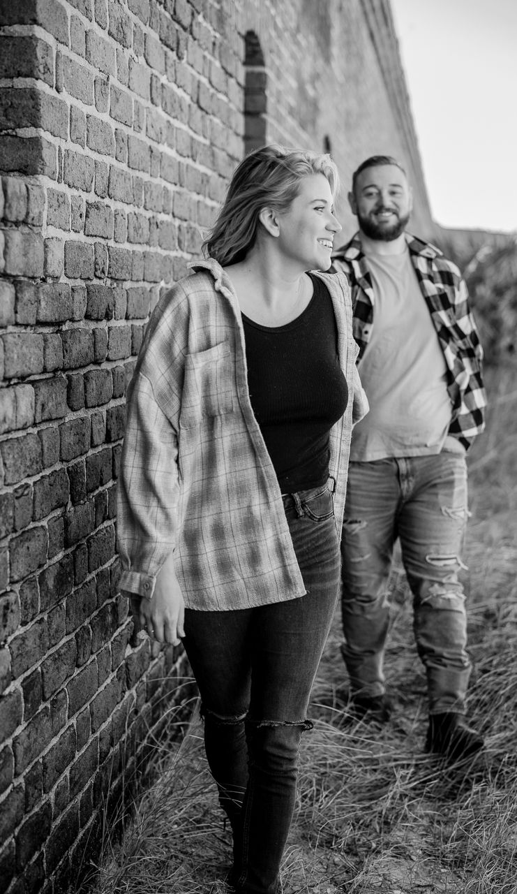 Black and white photos of a couple posing casually against a brick wall outdoors.
