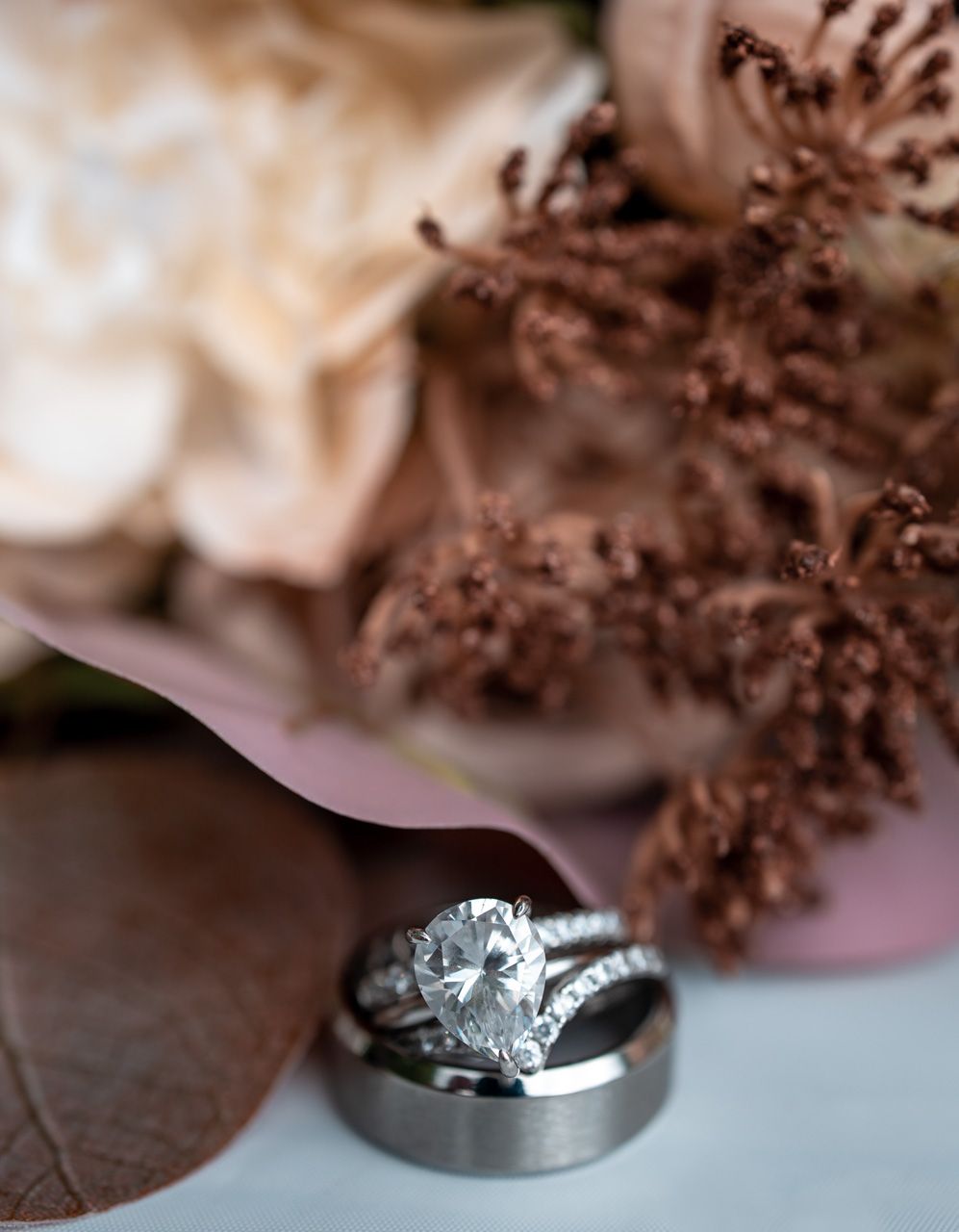 Wedding rings displayed with dried flowers and leaves in soft focus.