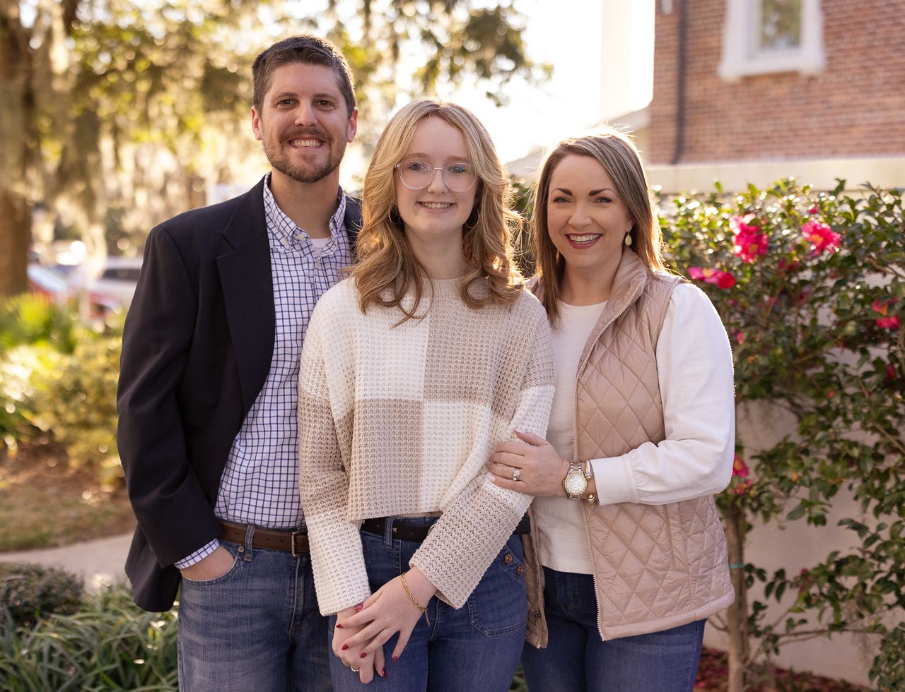 Family portrait session with coordinated neutral tones in front of brick and roses.