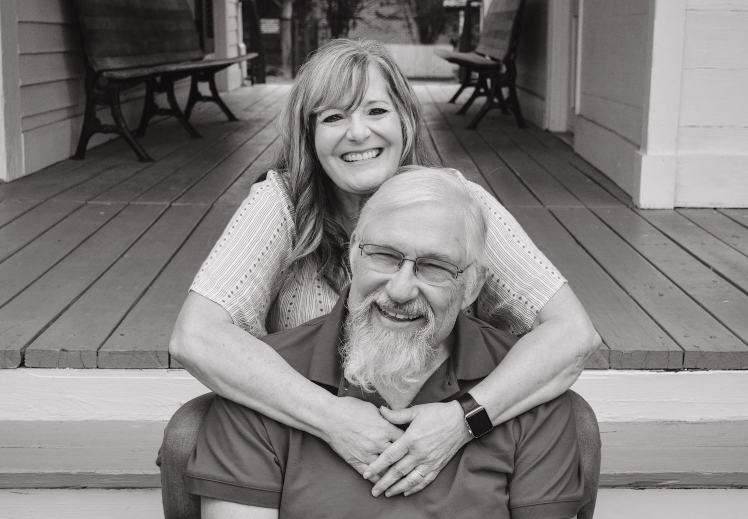 A heartwarming black and white portrait of two people sharing a moment on a wooden porch.