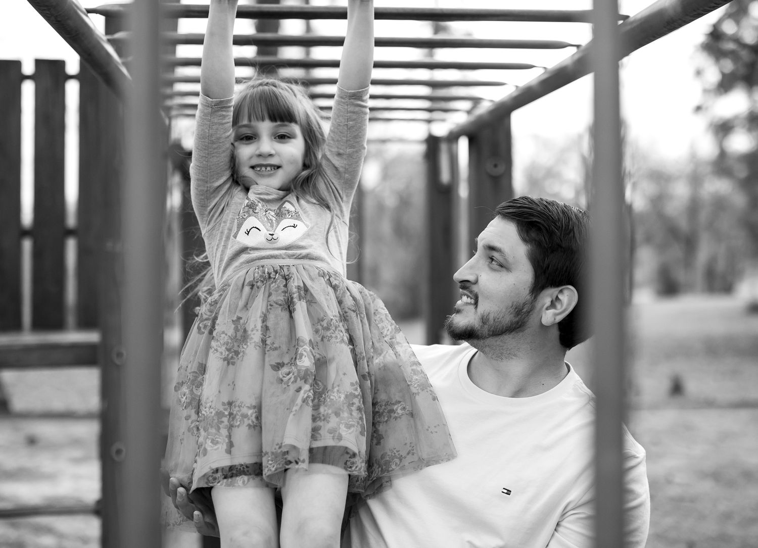 Family shares playful moments under architectural structure in black and white.