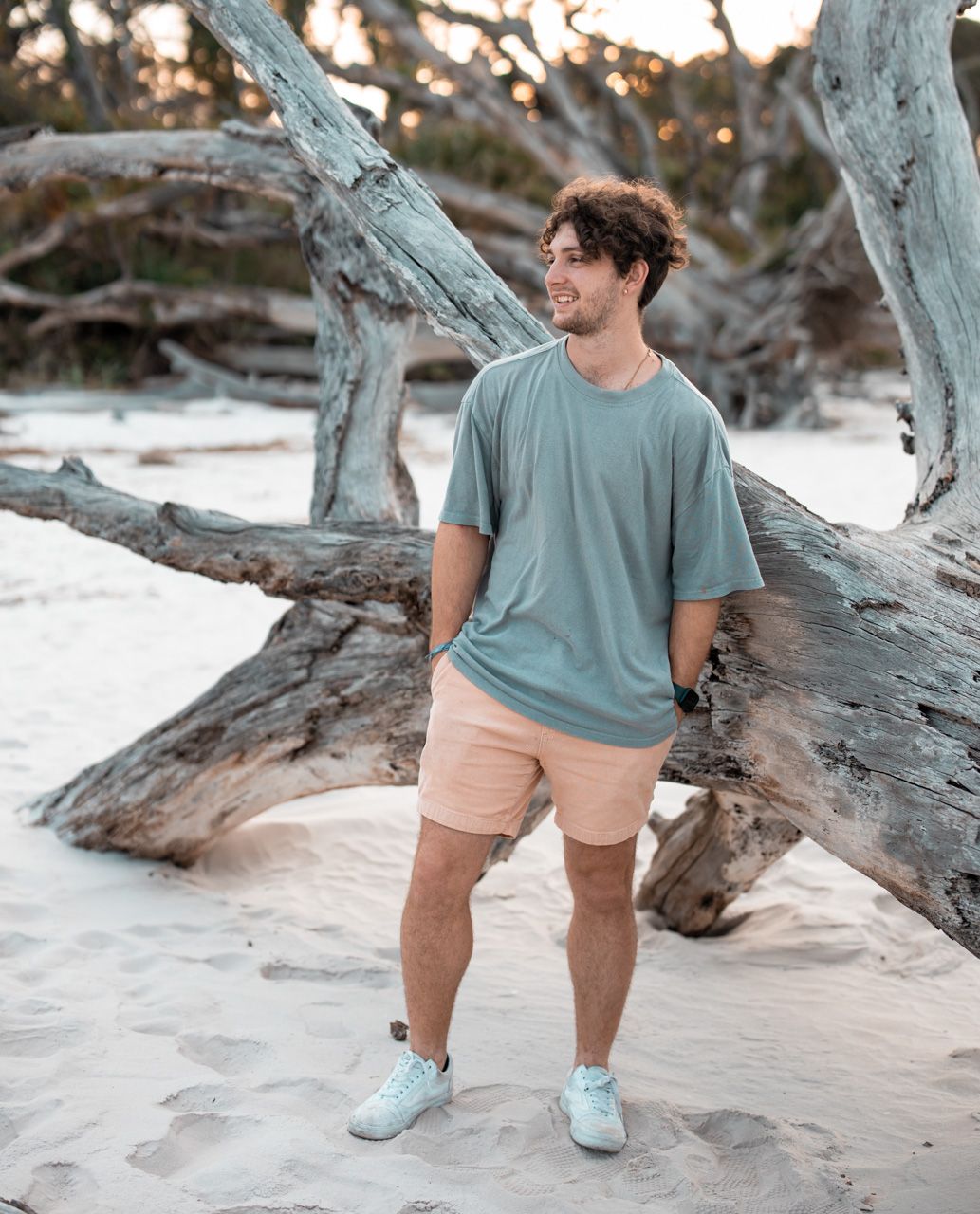 Casual beach portraits with teal shirt and khaki shorts against weathered driftwood.