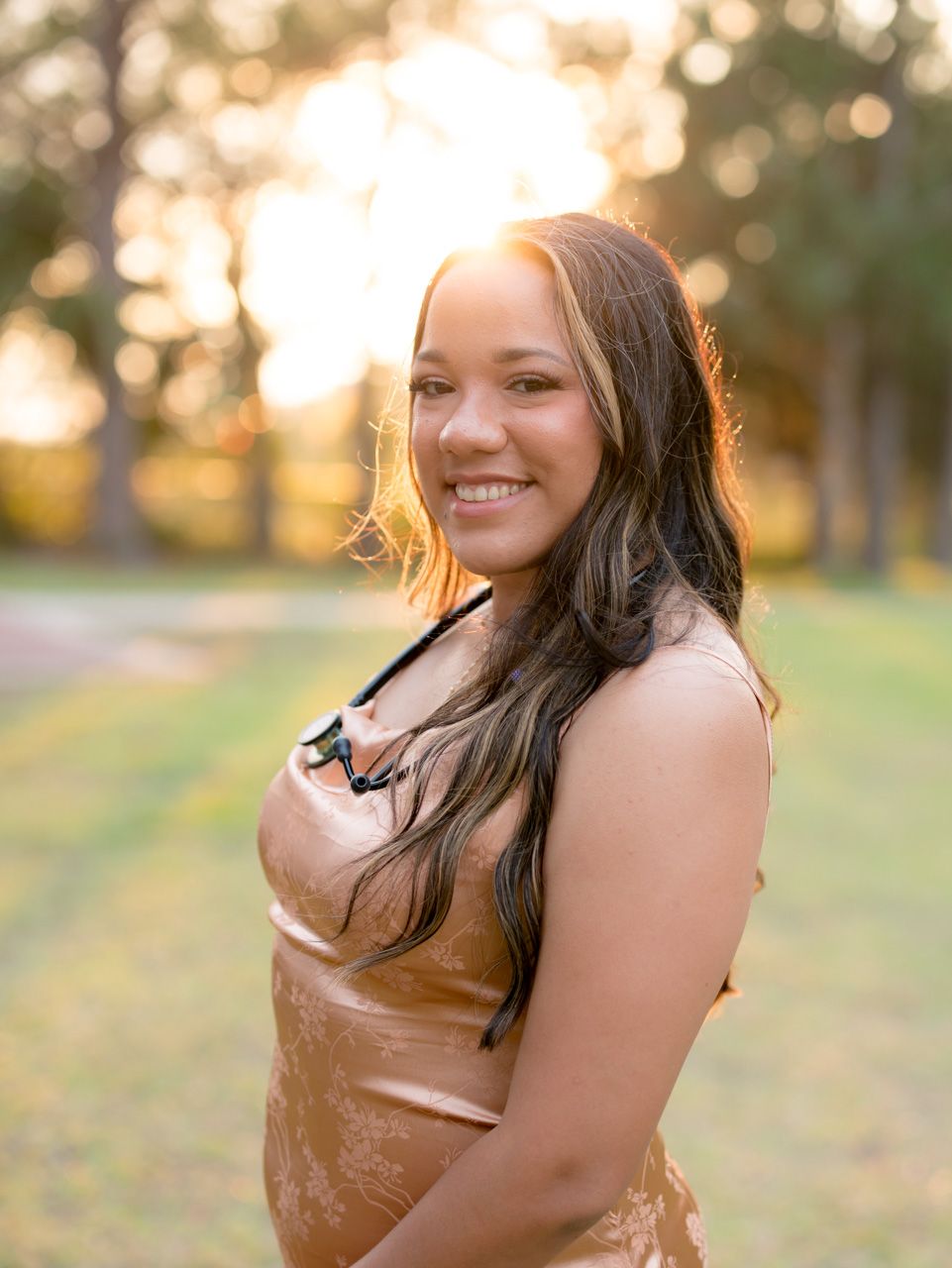 A portrait of someone in a golden dress with sunlit trees in the background.
