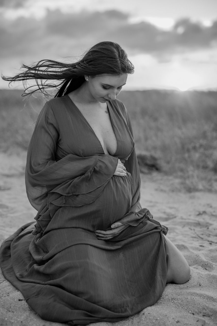 Artistic black and white maternity photos on a beach with flowing fabric and natural light.