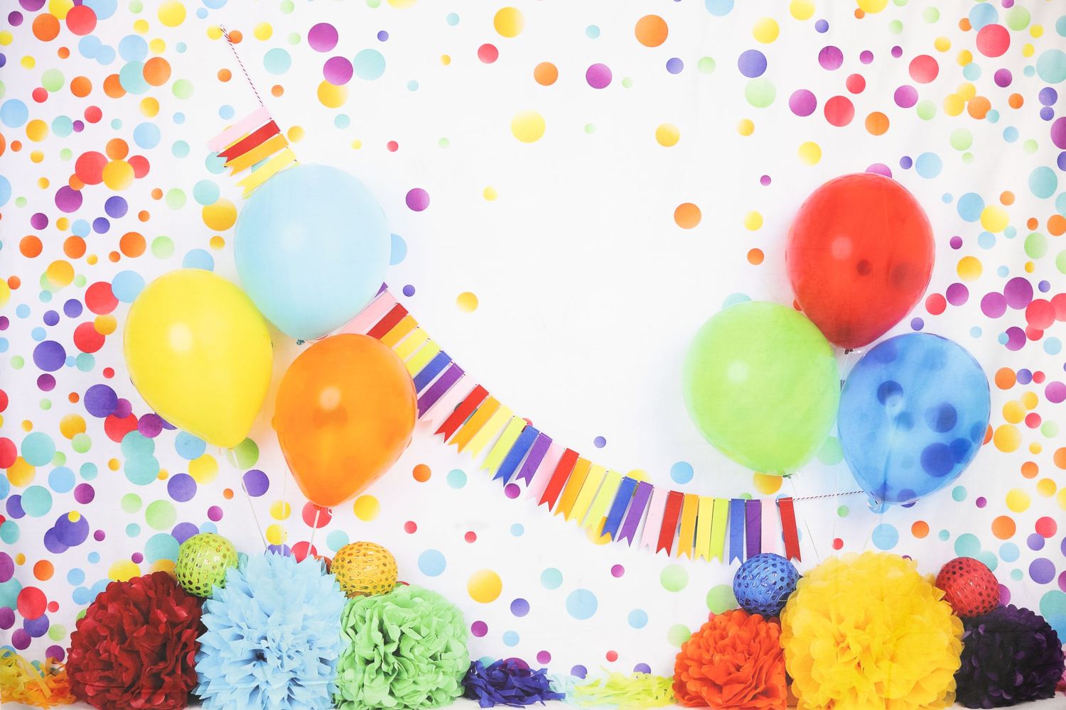 Colorful party scene with balloons, confetti dots, and tissue paper pom poms against white background.