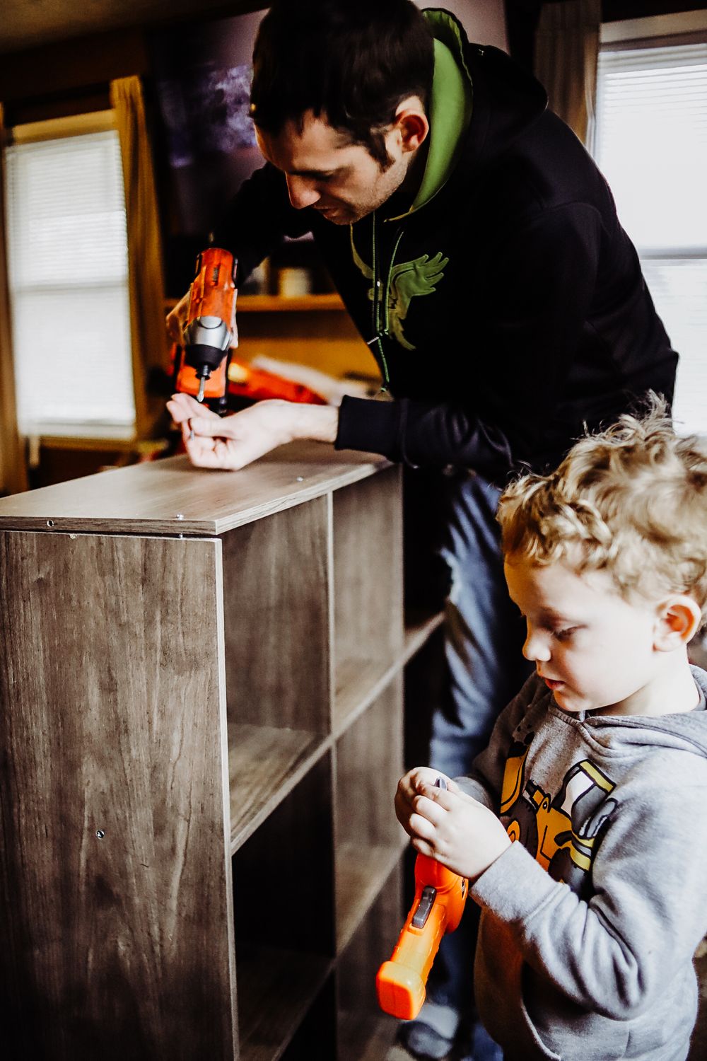 Parent and child playing with toys while organizing wooden shelving unit.