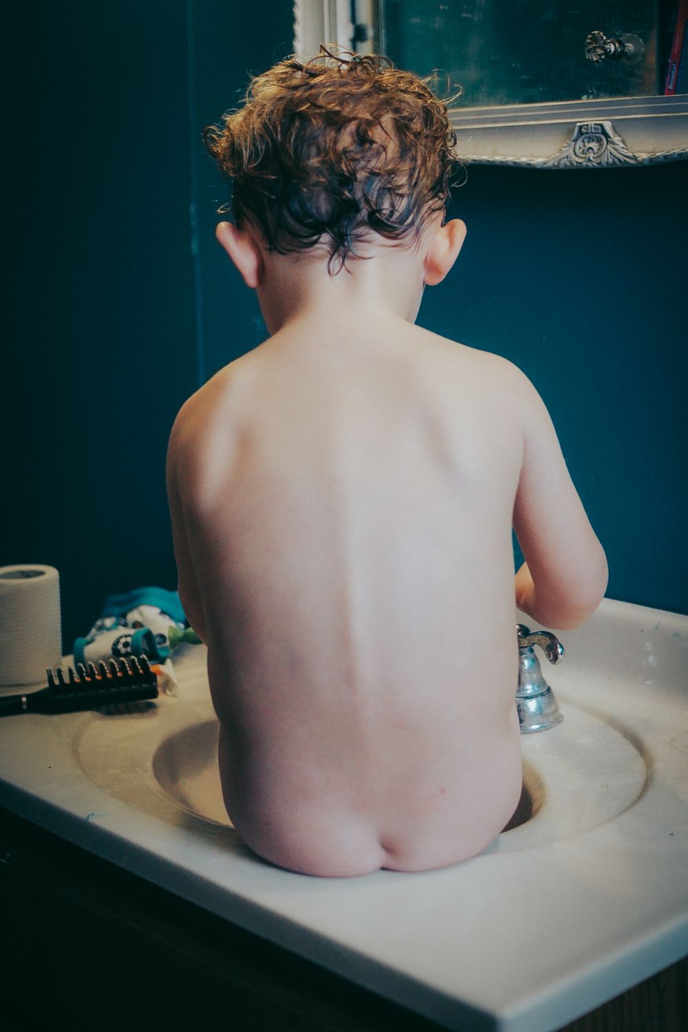 Child with curly hair sitting in a white bathtub against a dark blue wall.