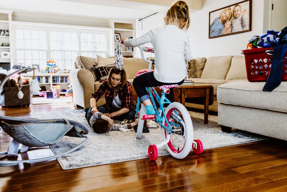 A small child rides a pink bicycle in a cozy living room with hardwood floors and beige furniture.
