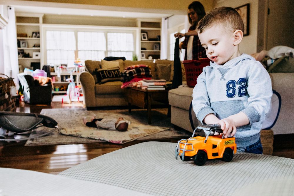 Young child playing with orange toy truck on grey couch cushion.
