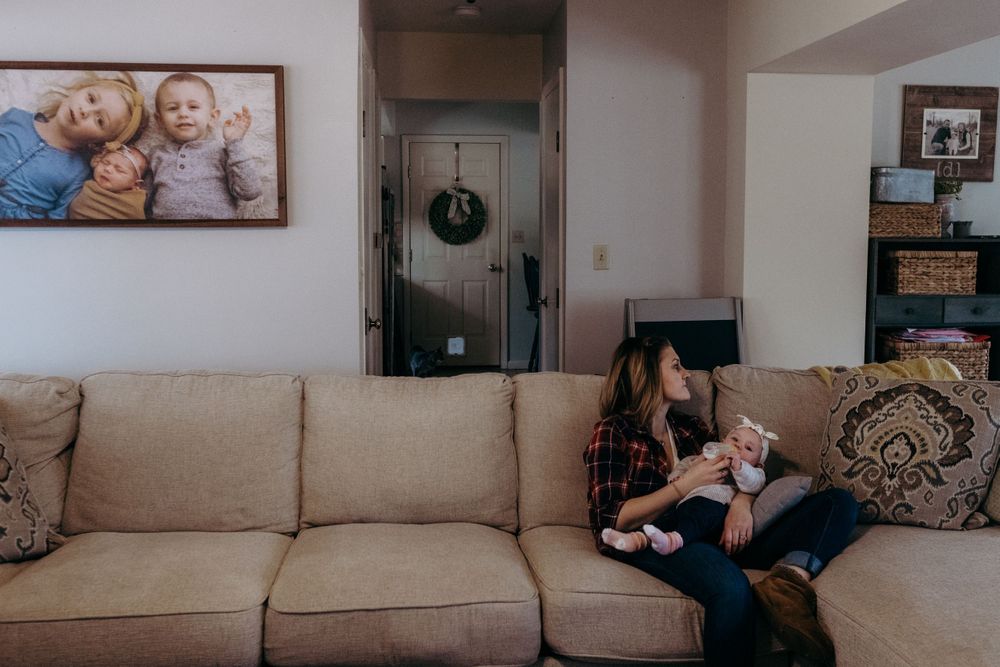 Cozy living room with beige sofa, framed photos, and wreath visible in hallway.