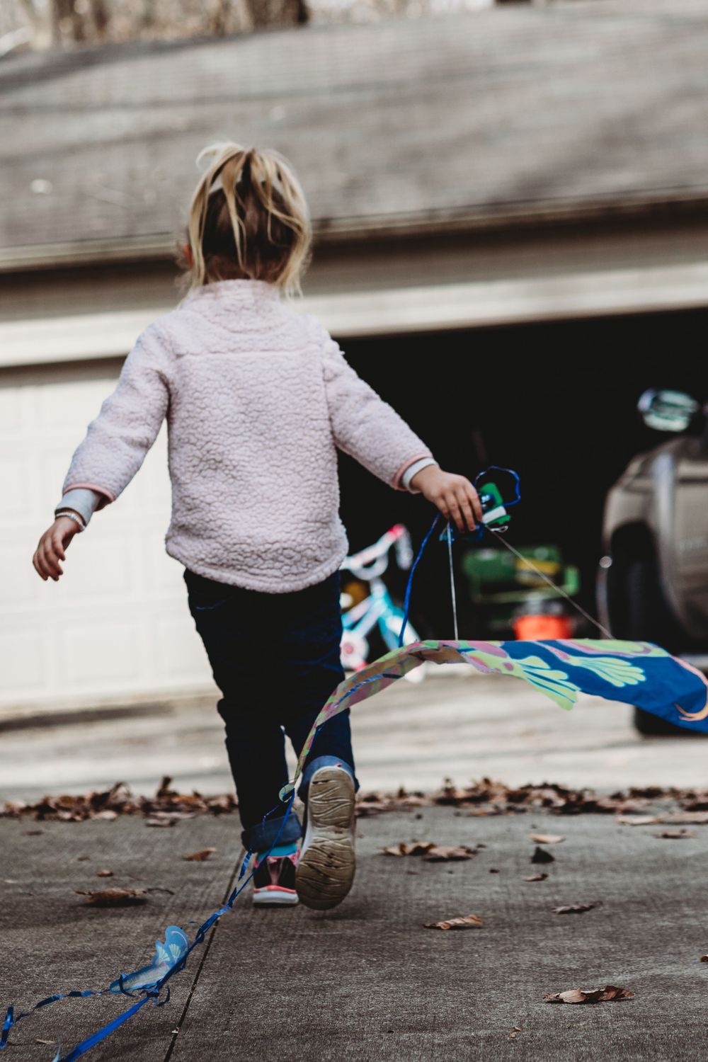 A small child in a fuzzy sweater playing with colorful streamers on a driveway.