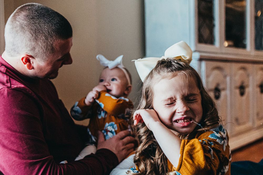 Family moment in living room with young children wearing bows and playing.