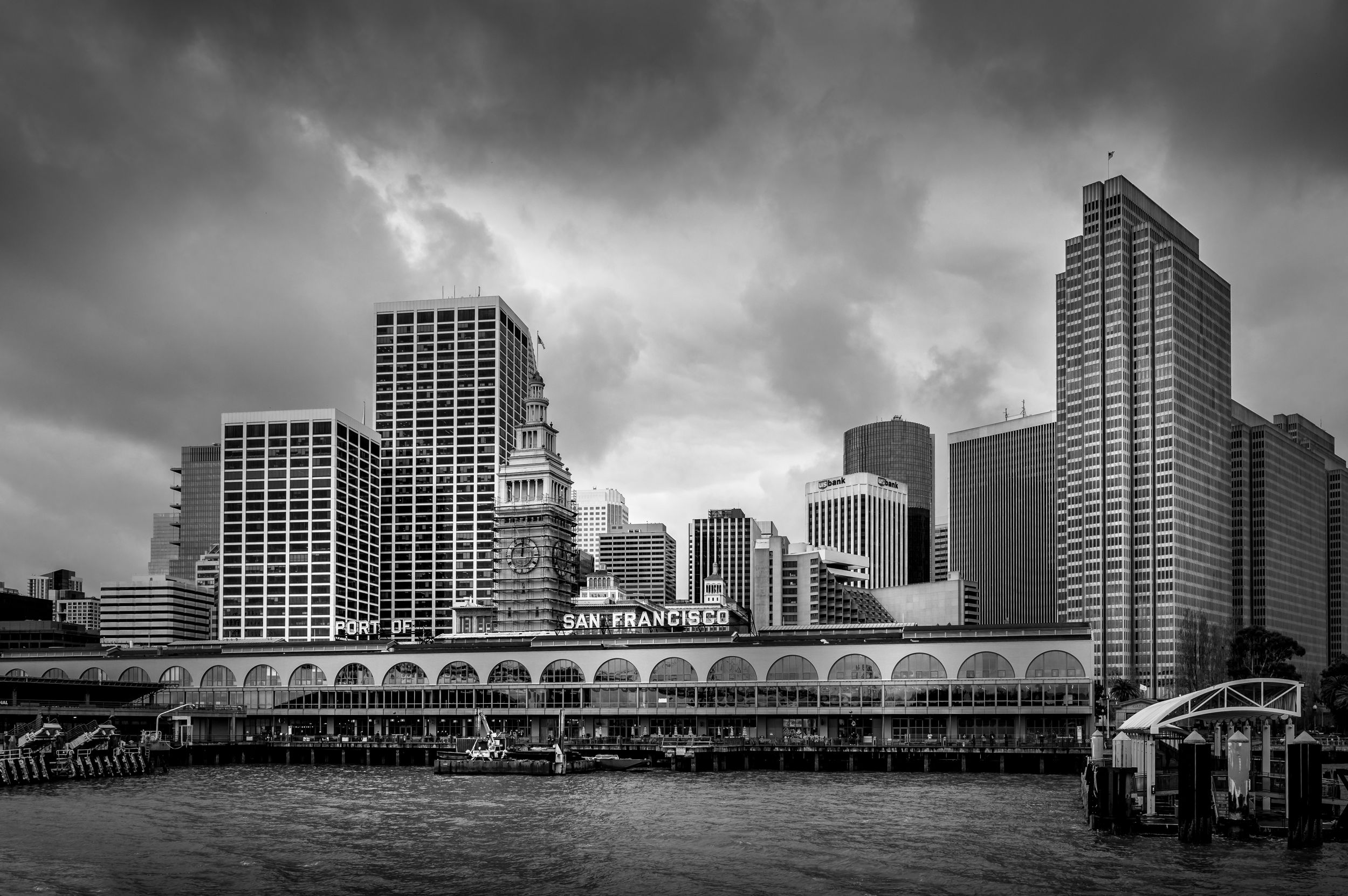 Dramatic black and white cityscape of San Francisco's Financial District with pier and moody storm clouds.