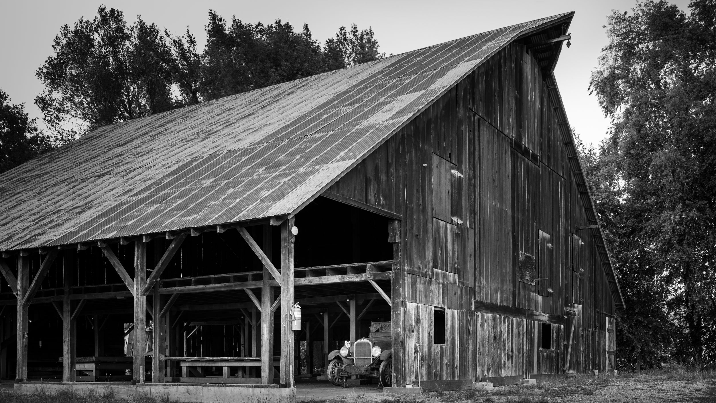 Black and white photograph of a weathered wooden barn with rustic beams and a slanted roof.