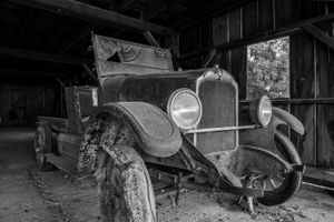 Antique automobile covered in dust inside an old wooden barn.
