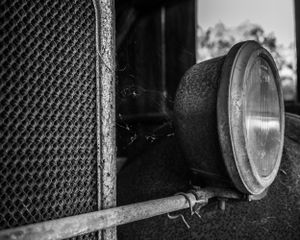 Side view of vintage car headlamp and radiator grille in black and white.