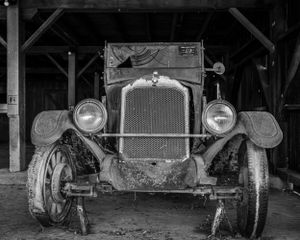 Front view of weathered vintage automobile in barn with dual headlights.
