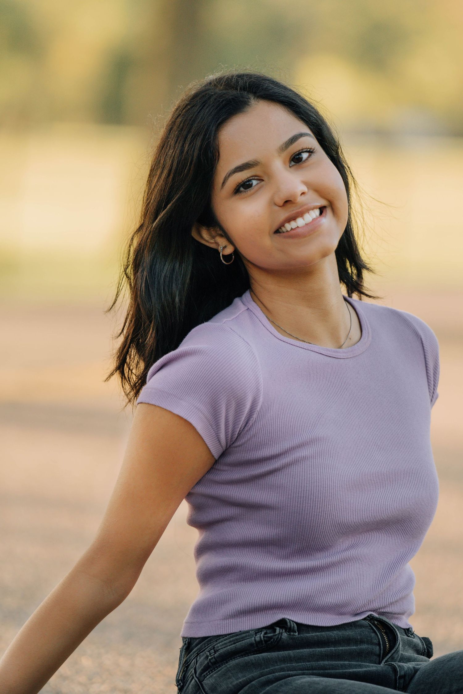 Person in purple shirt poses playfully against warm outdoor background.