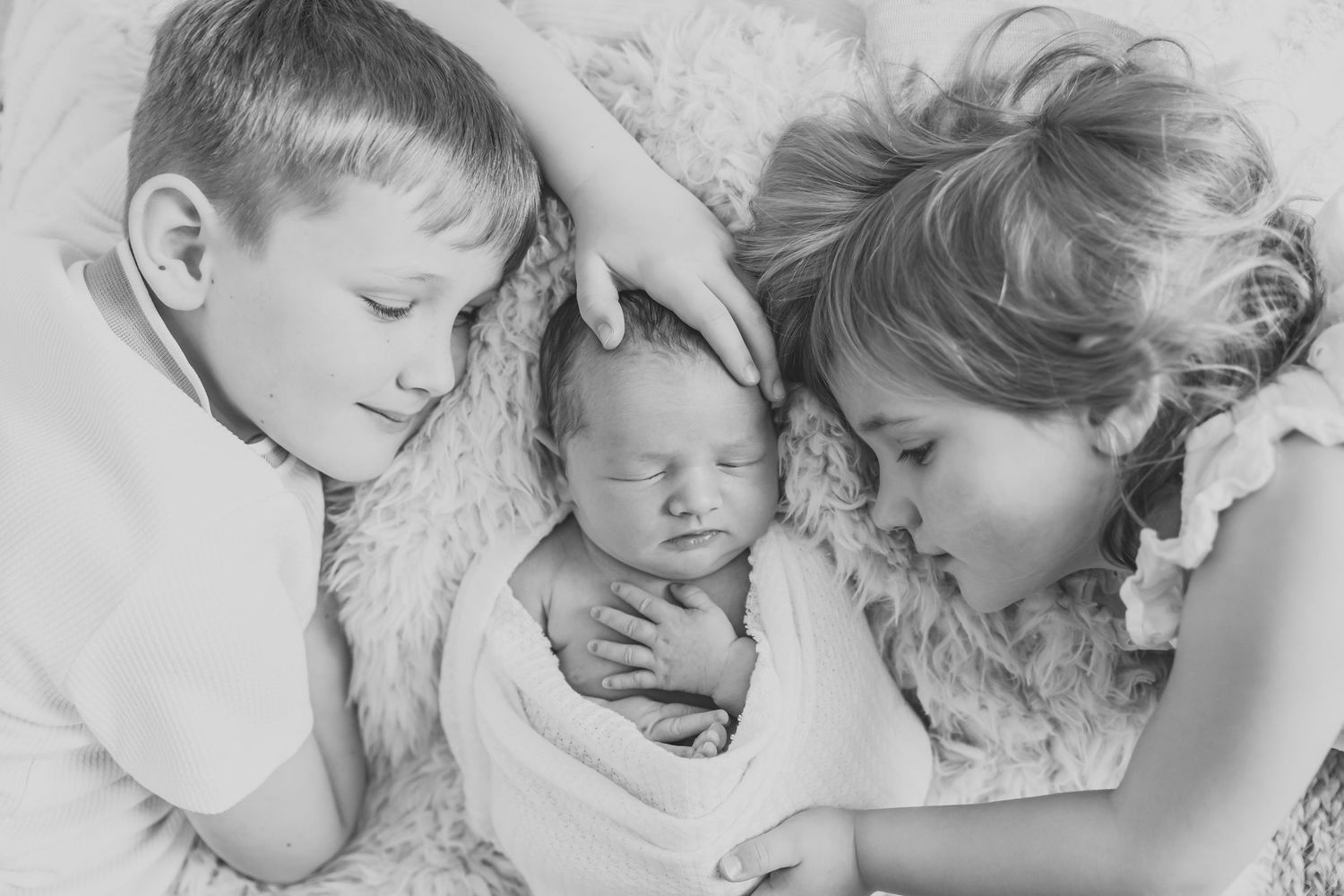 Three children rest peacefully together on white bedding in black and white.