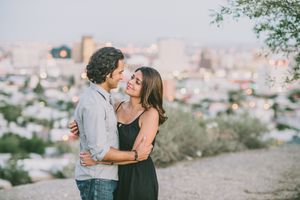 Casual engagement portrait of couple overlooking city skyline at sunset.