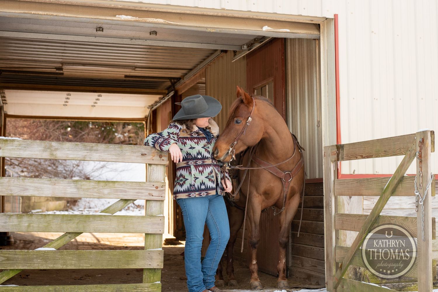 A beautiful brown horse stands in a barn stall with wooden fencing.